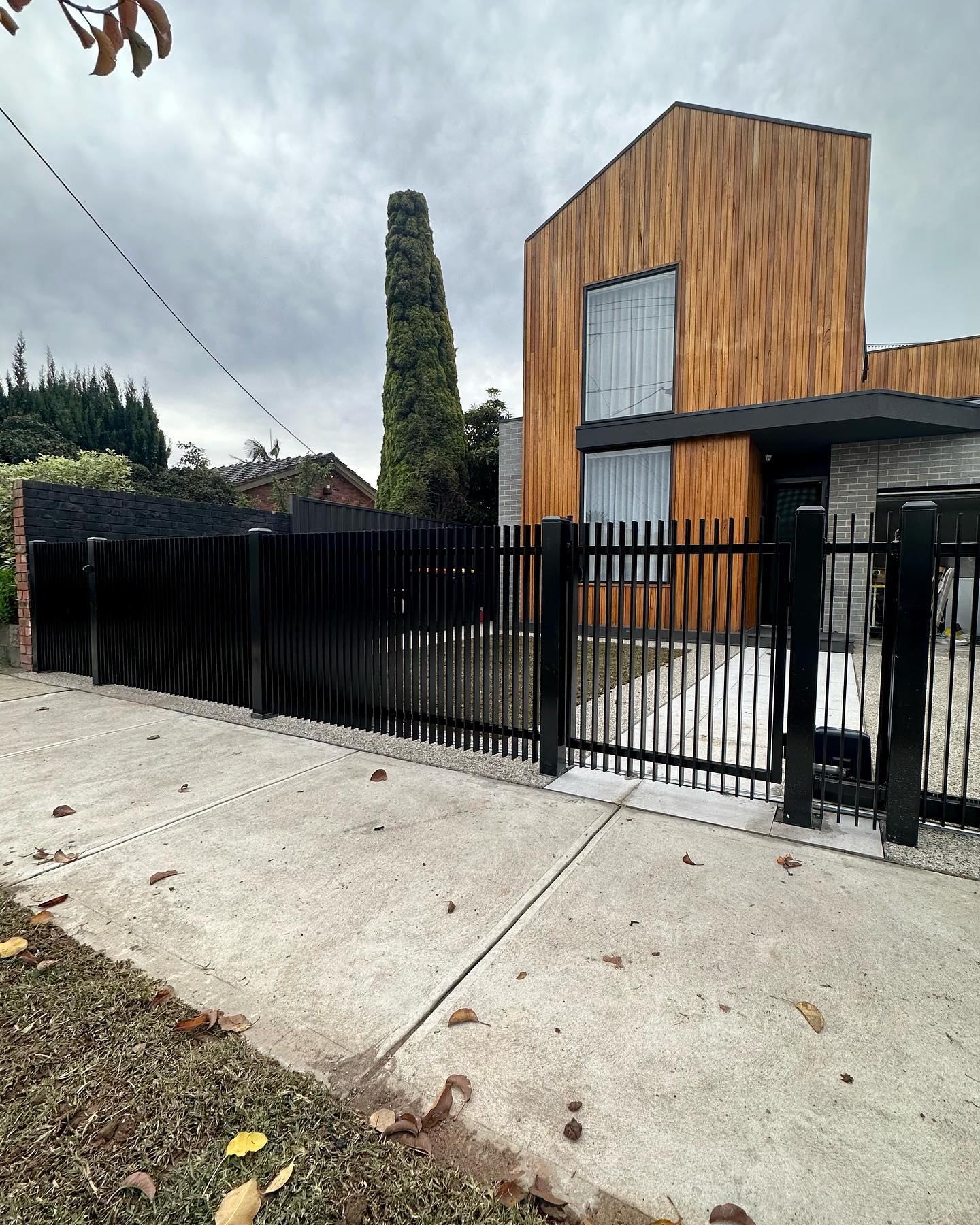 Modern residential house with wooden facade behind black metal fence