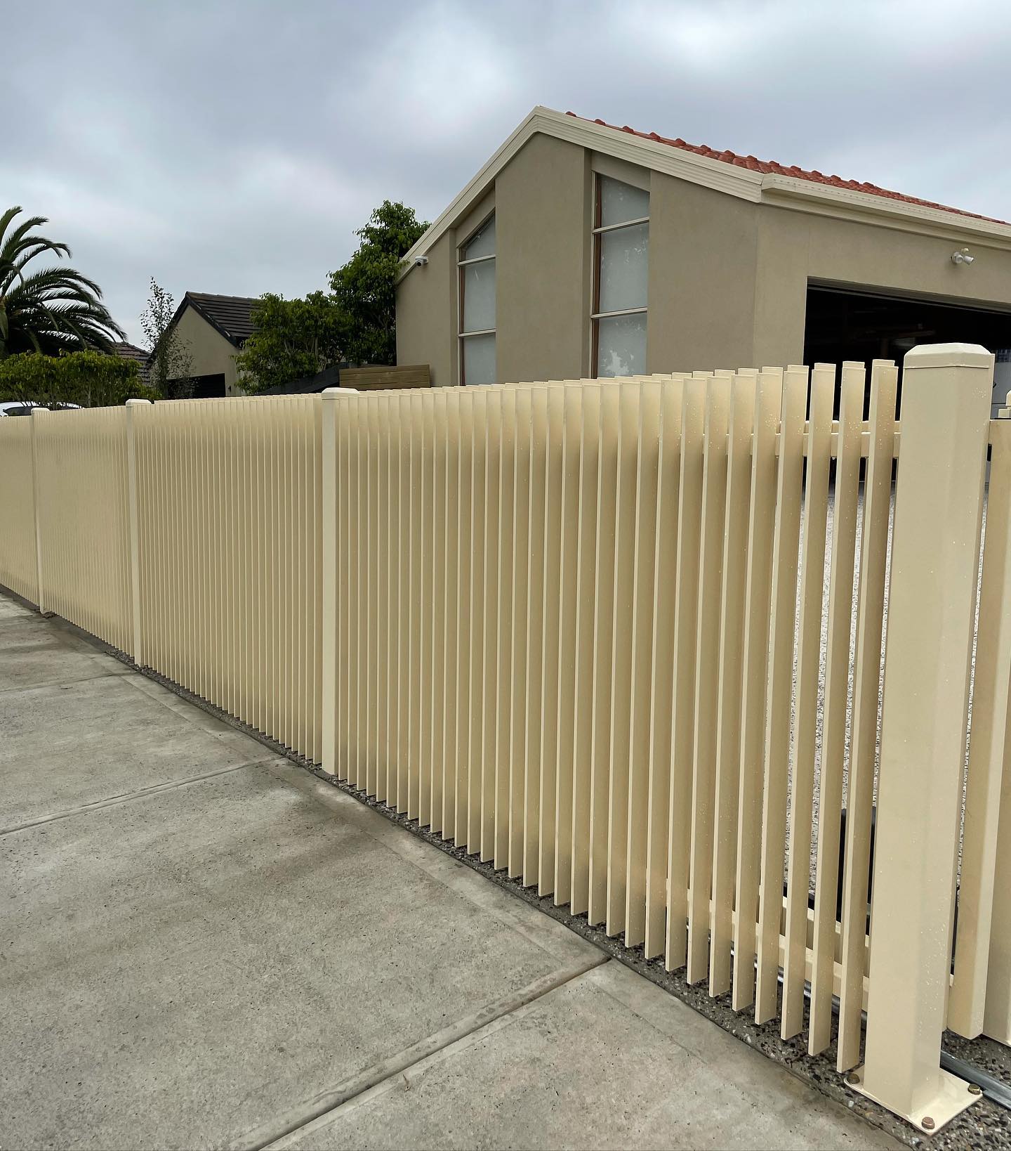 Beige automated gate system with vertical slats along concrete pathway