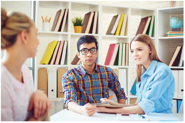 Three colleagues engaged in a discussion at a table within an academic environment, demonstrating the dynamics of peer interaction during observation feedback sessions.
