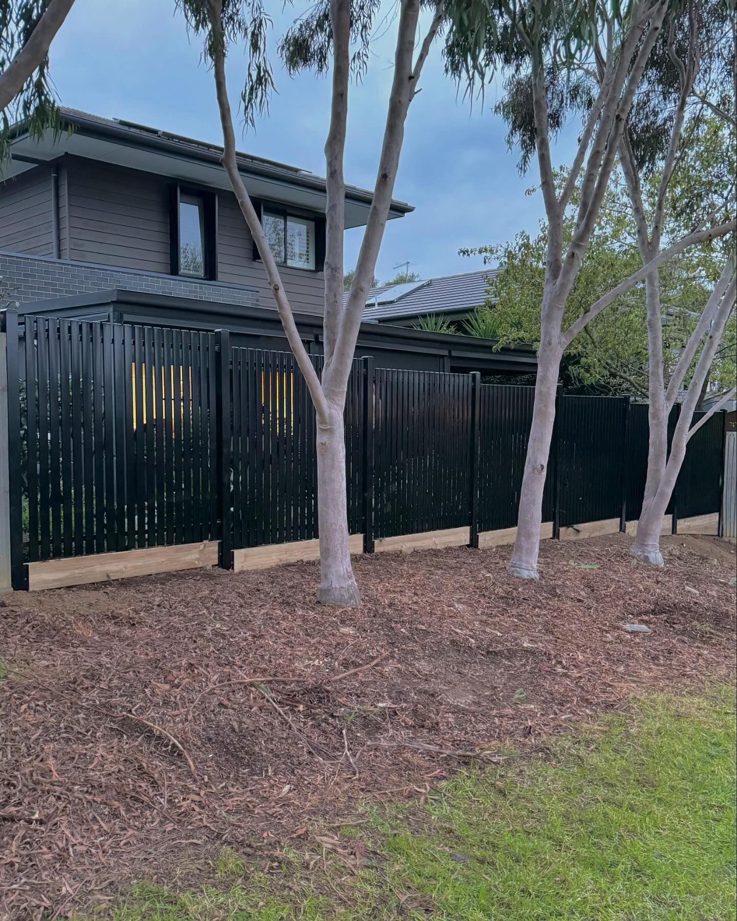 Flat Top Picket fence running parallel to house with trees in foreground