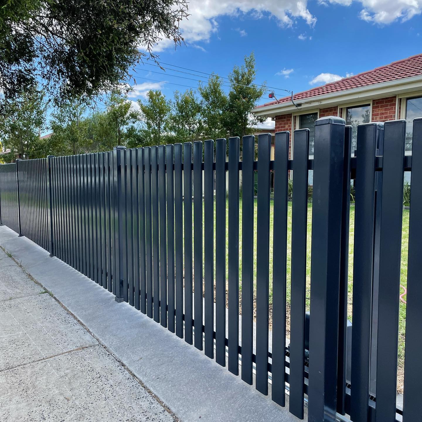 Newly installed black metal fence mounted on concrete base