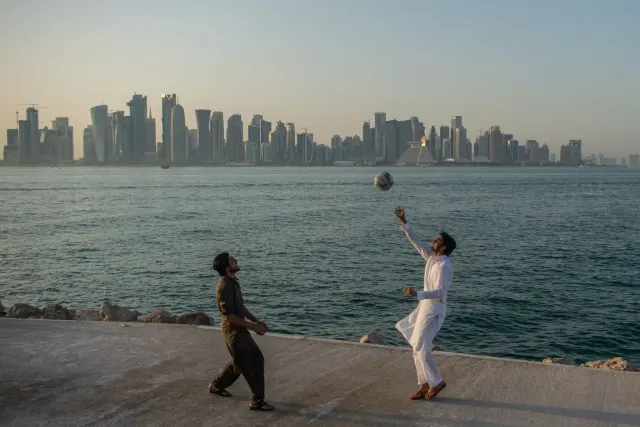 Expat playing football on the Doha Corniche with the West Bay skyline towers in the background overlooking the waterfront.
