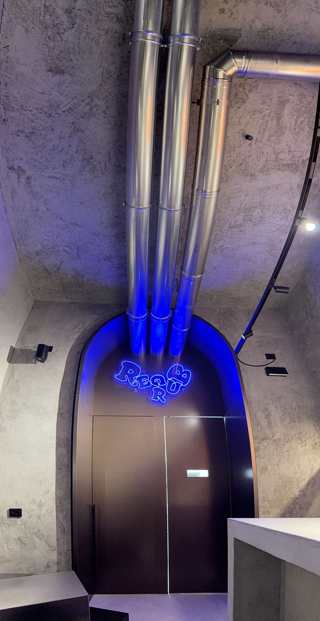Interno moderno con tubi metallici, porta ad arco con illuminazione blu e insegna al neon "ReQB".