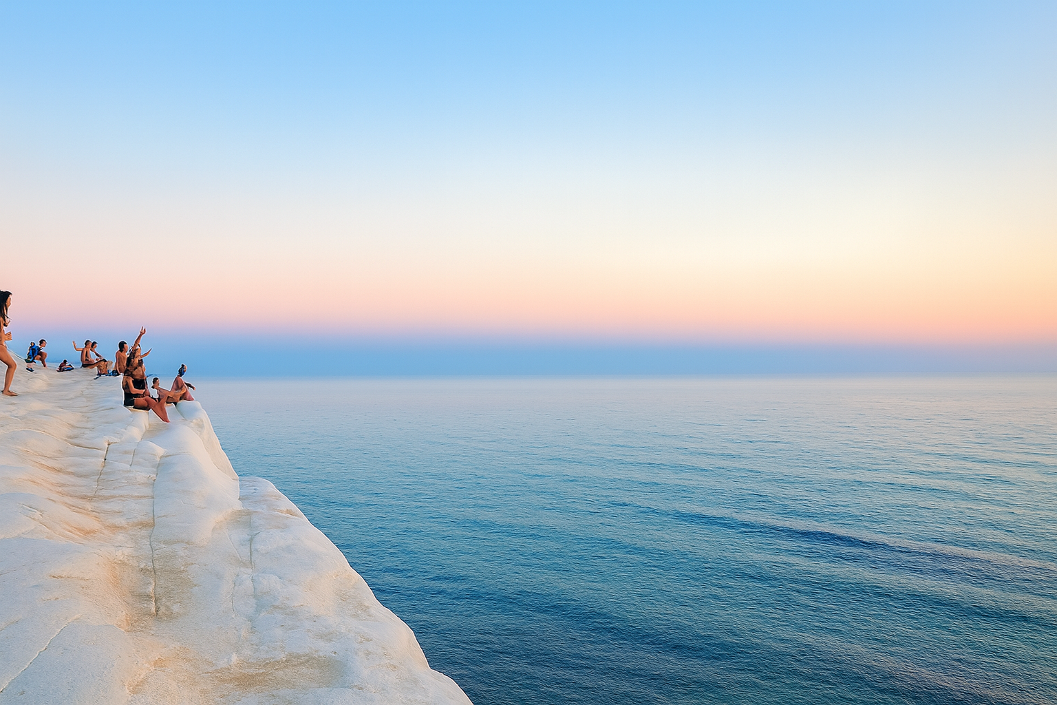 A group of people sitting on white cliffs overlooking the ocean at sunset.