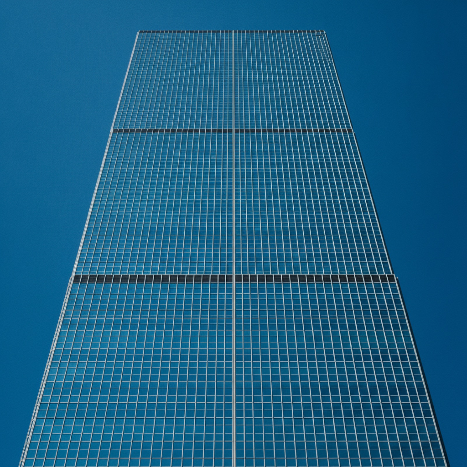 High-rise commercial tower clad in reflective curtain wall with a precise multi-story mullion grid against a blue sky