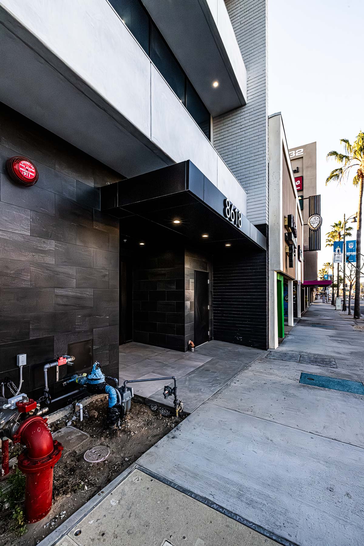 A modern commercial building entrance with dark tiled walls, a black awning, and upper-level windows, seen from the sidewalk.