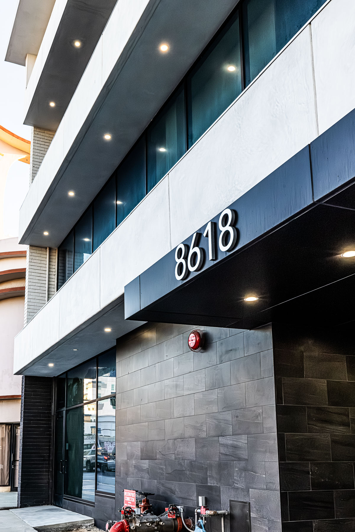 A modern building facade featuring large glass storefront windows, dark aluminum panels, and the address number 8618.