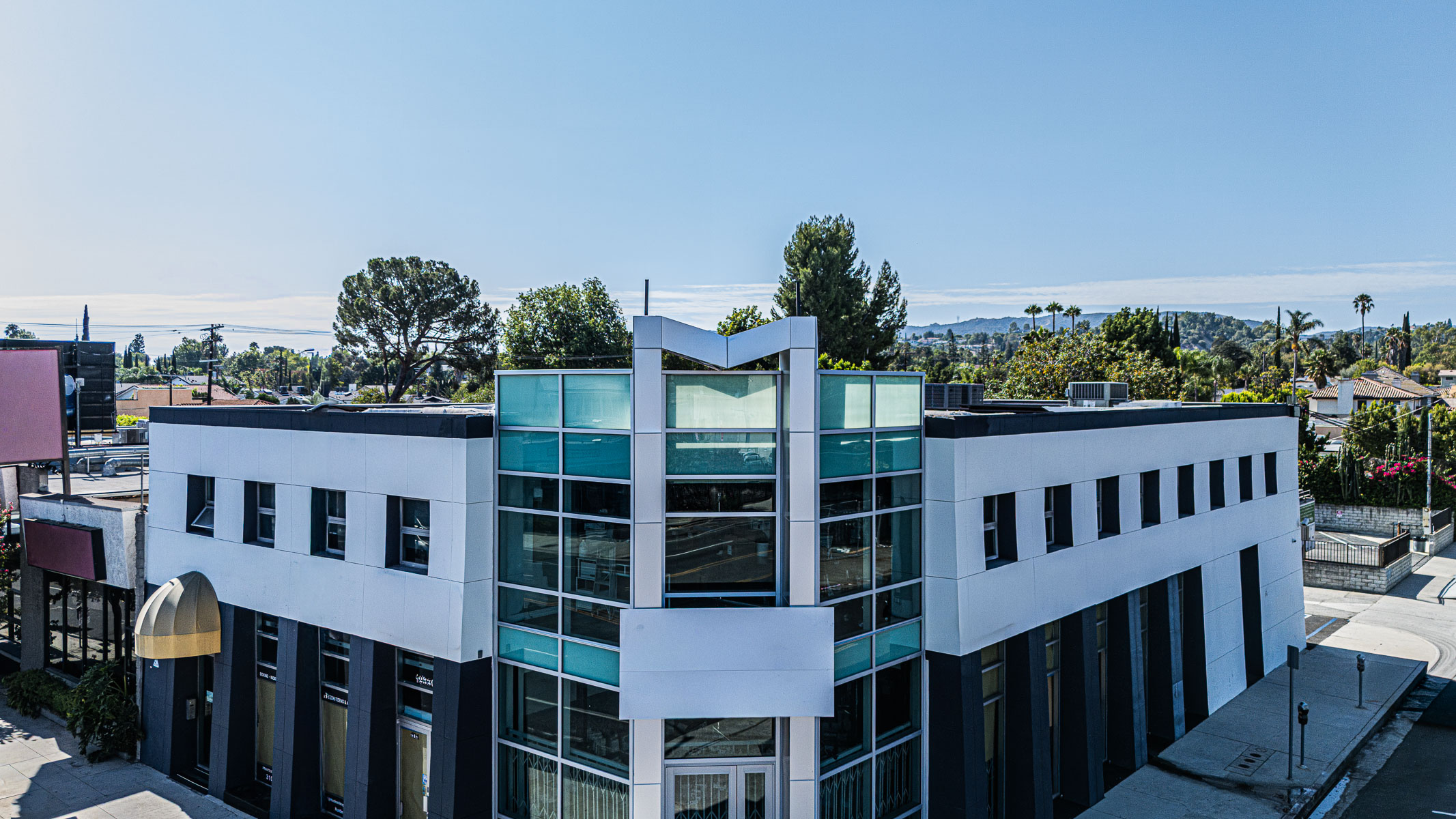An elevated exterior view of a commercial building featuring a new glass curtainwall at its corner under a clear blue sky.