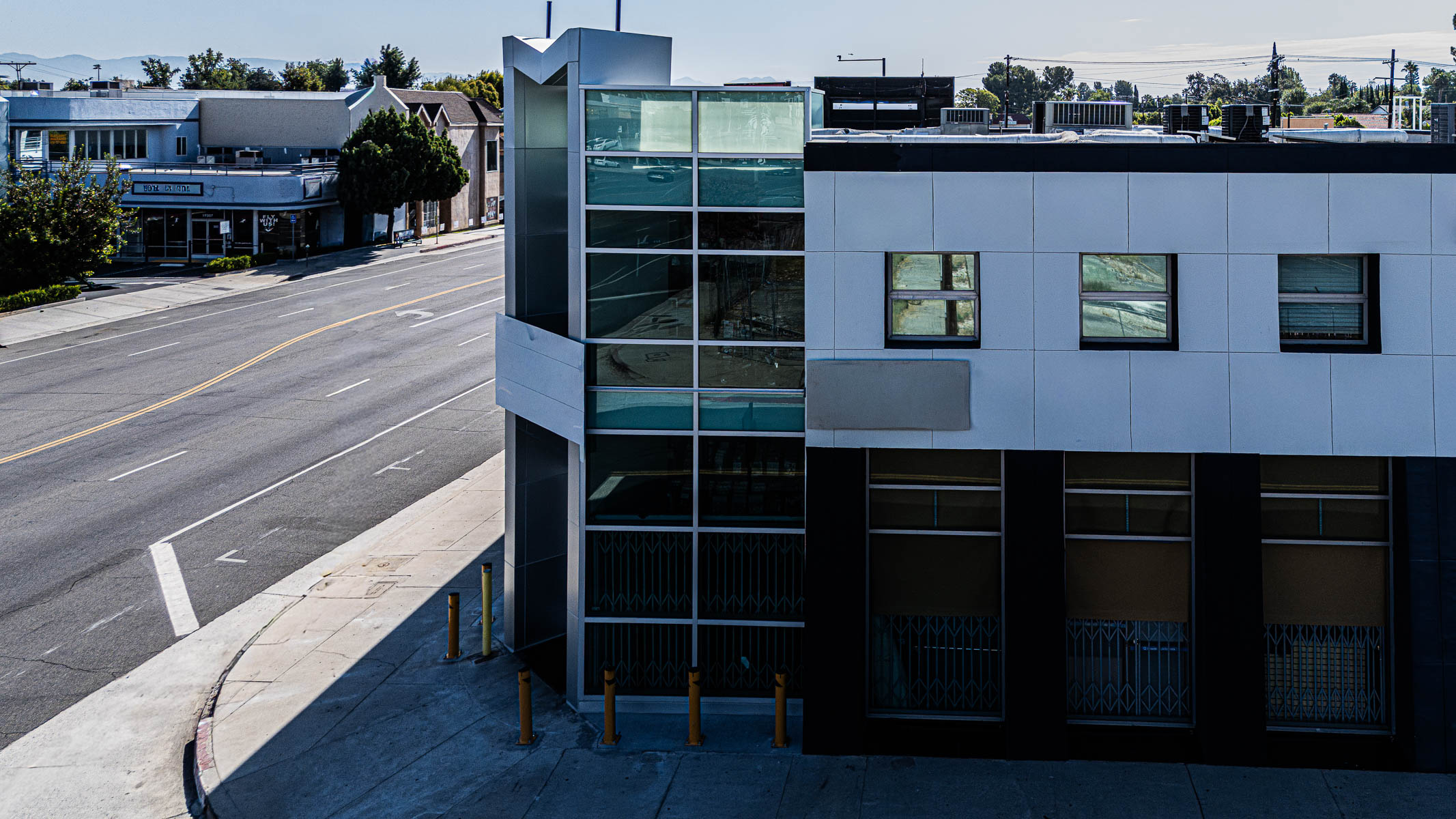 An exterior view of a commercial building at a street corner featuring a new multi-story glass curtainwall, with a street and sidewalk visible.