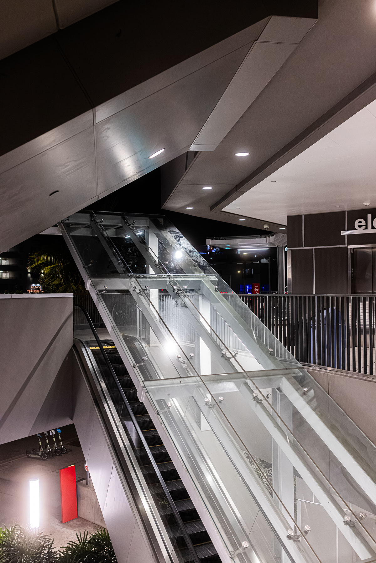 An exterior view of an escalator entrance with a clear tempered laminated glass canopy at night.