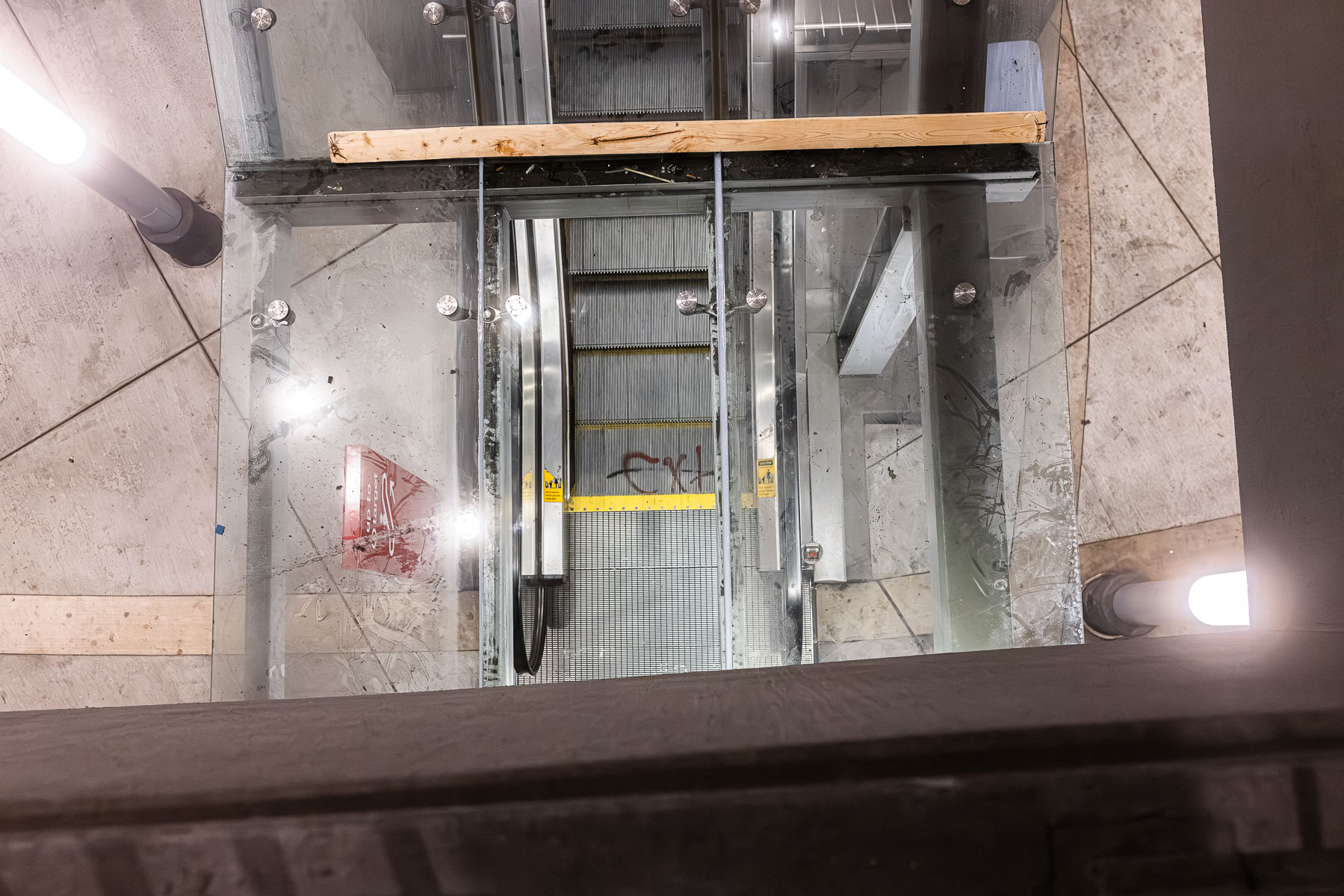 A view looking down through clear glass canopy panels towards an escalator entrance.