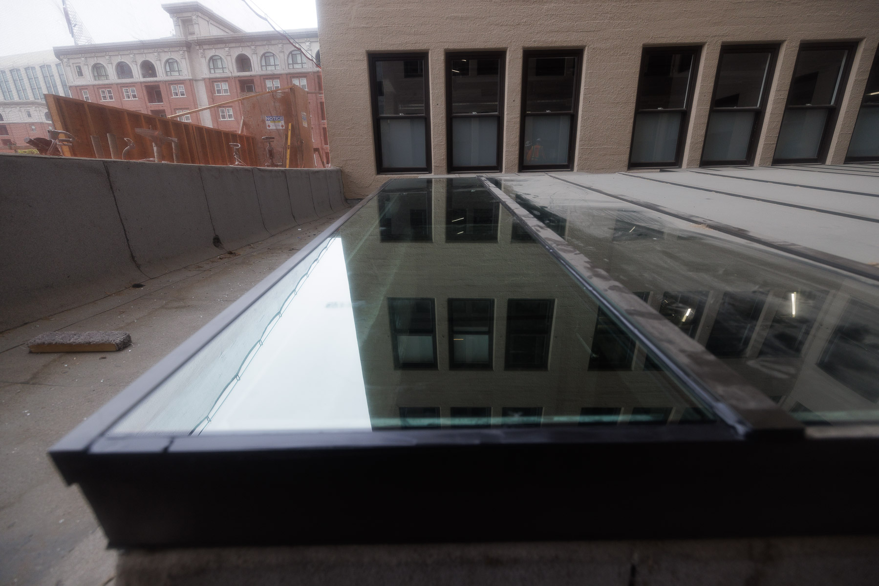 An exterior view of a newly installed glass skylight reflecting an adjacent building with windows.