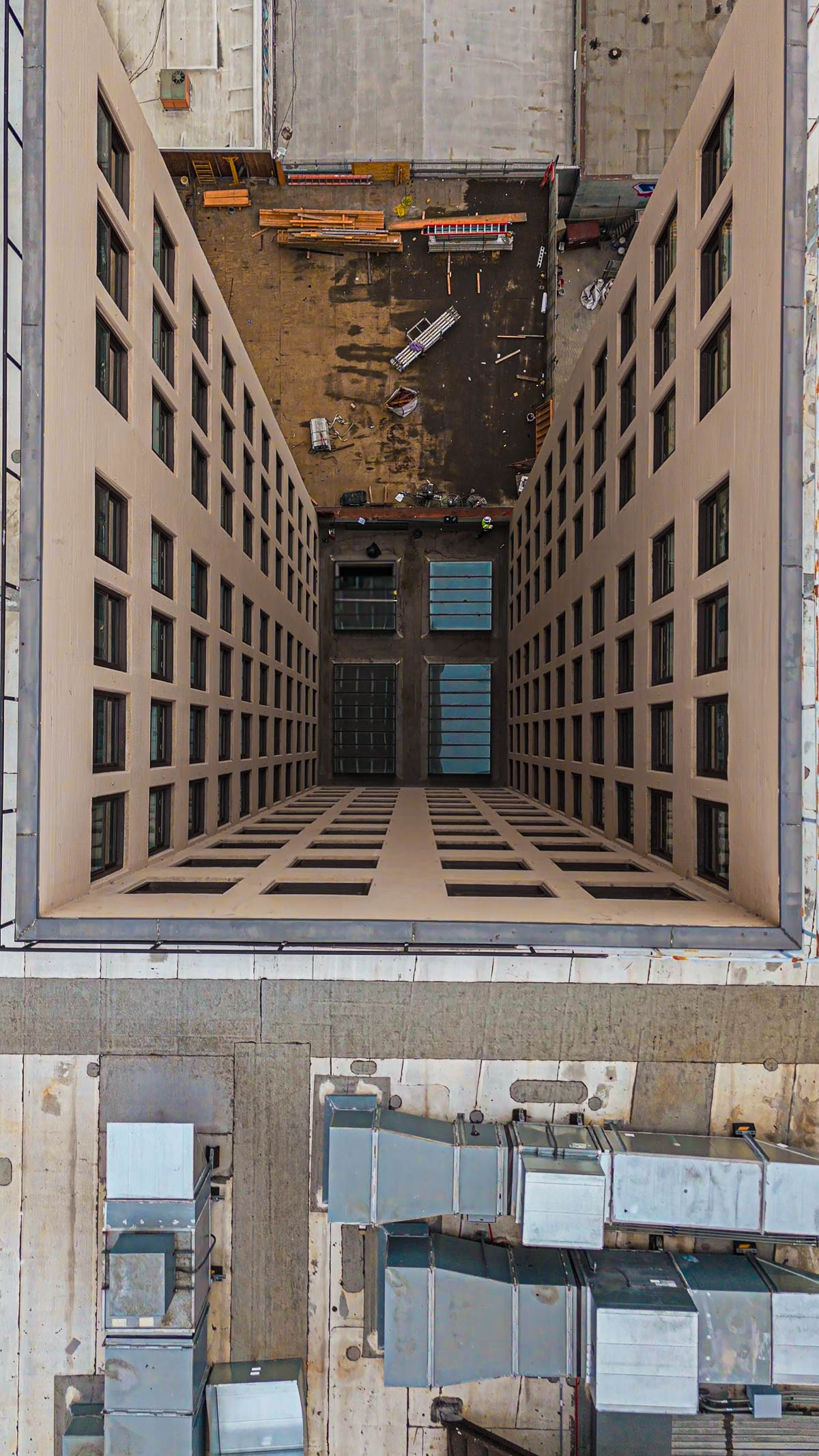 An aerial view looking down into a light well between two commercial buildings, showing four skylights at the bottom, two of which appear newly installed.