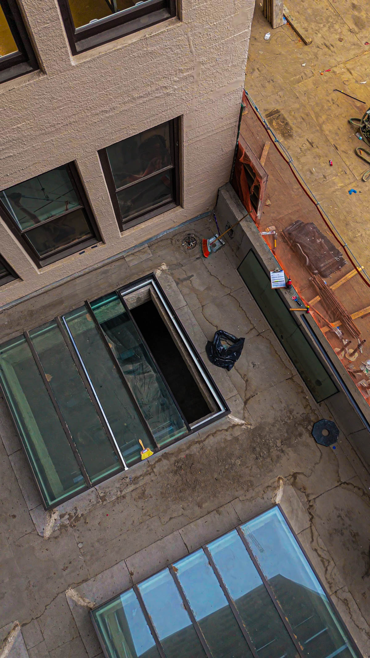An aerial view of a building rooftop shows a skylight with several glass panels installed and one section open, revealing the building's interior.