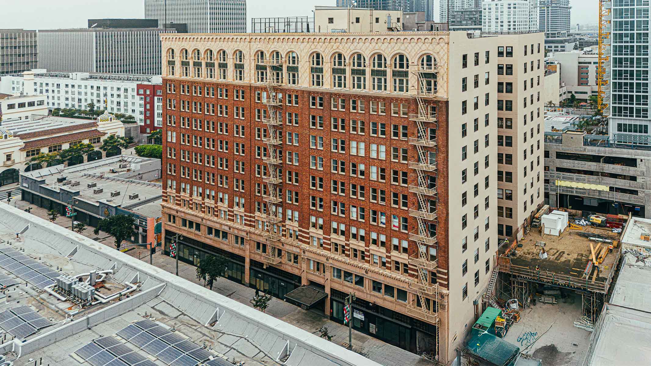 An aerial view of a multi-story brick commercial building with arched windows and fire escapes in a dense urban setting.