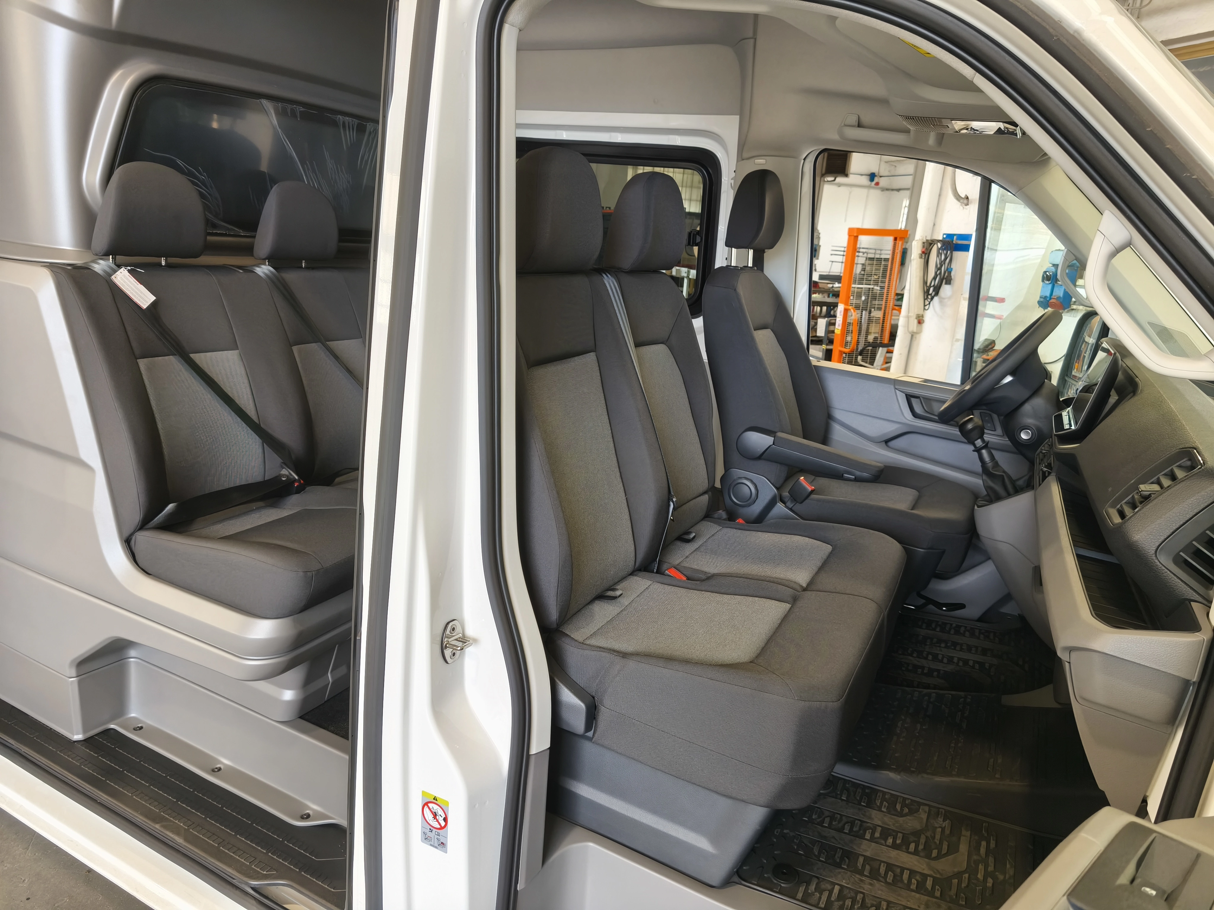 Interni di un furgone con tre file di sedili grigi.