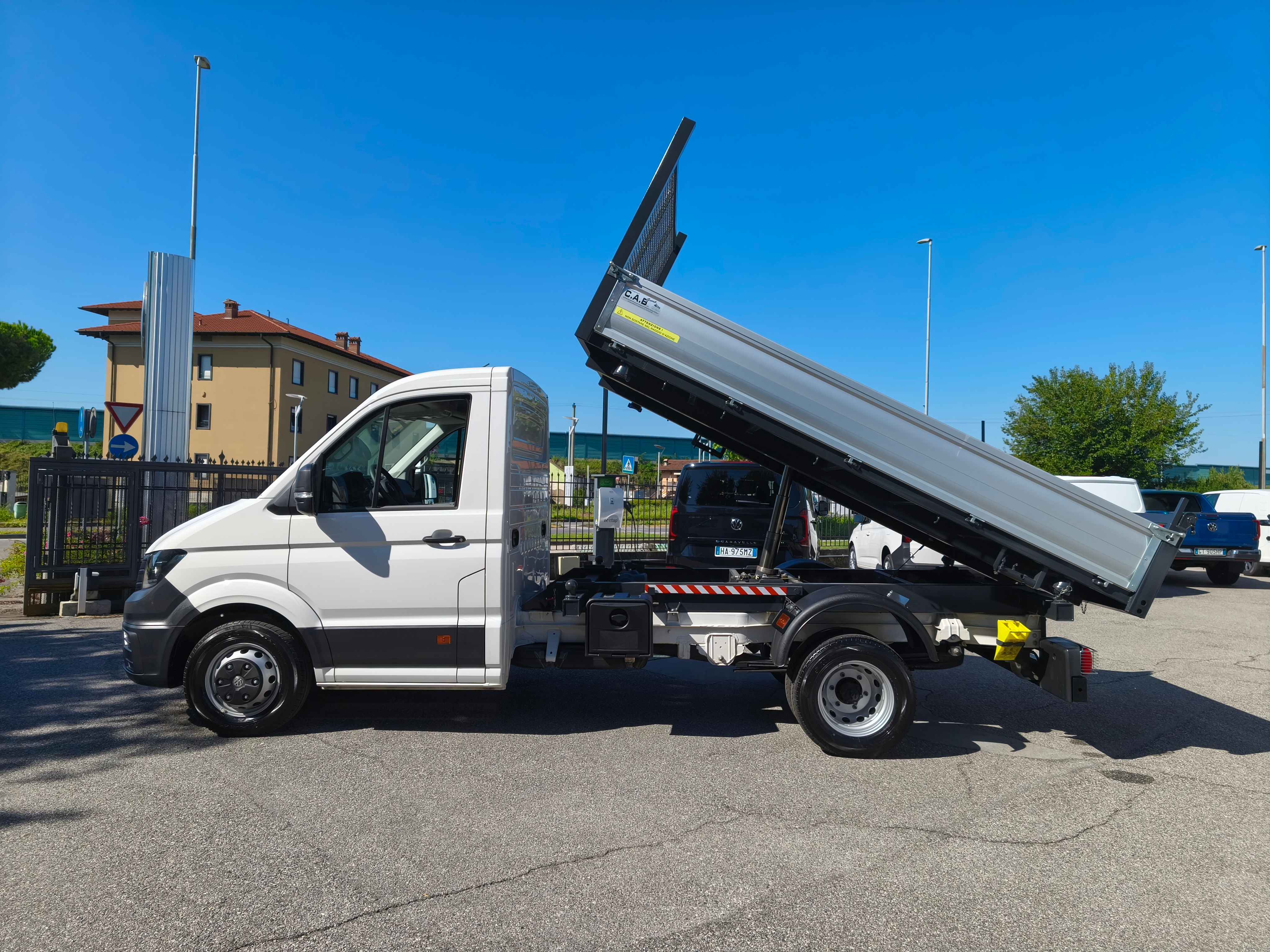 Camion ribaltabile bianco con cassone ribaltato, parcheggiato su asfalto sotto un cielo azzurro.