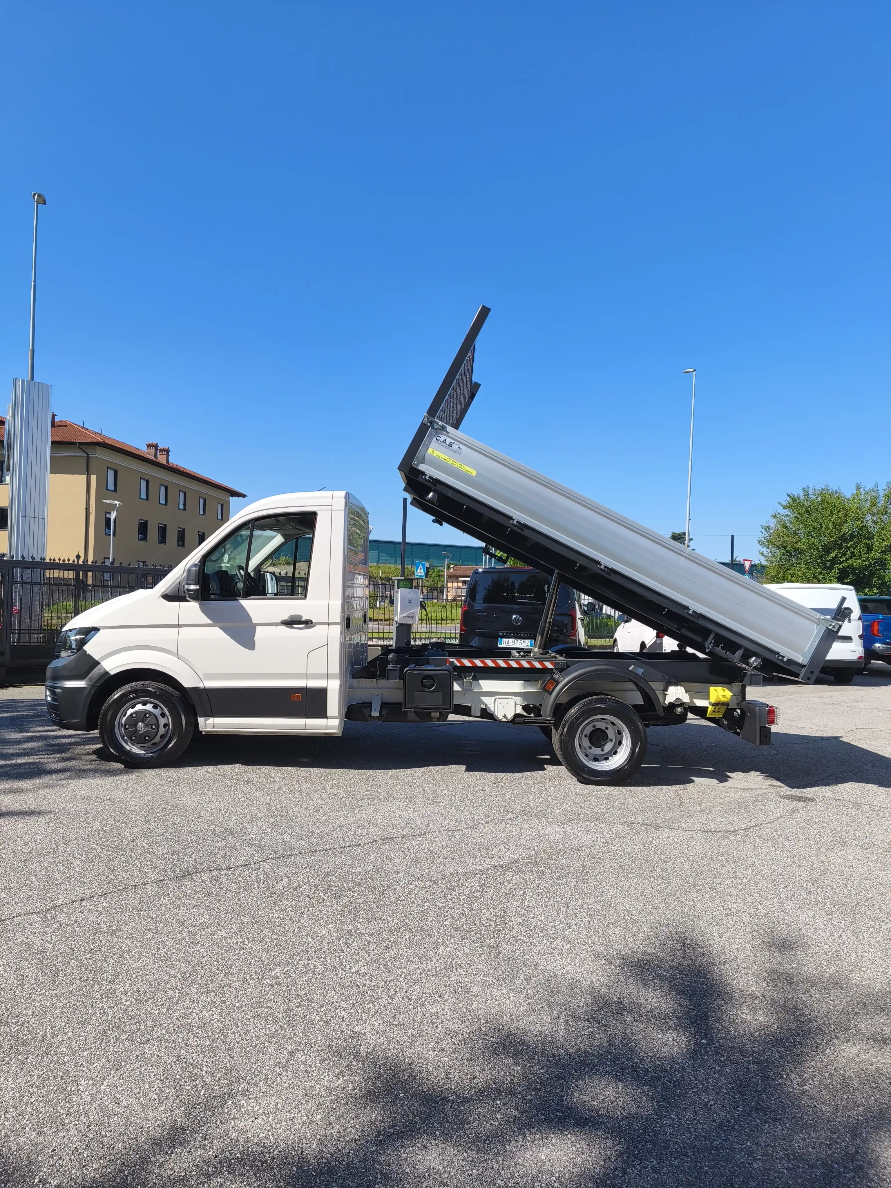 Camion ribaltabile bianco con cassone sollevato su asfalto. Cielo blu.