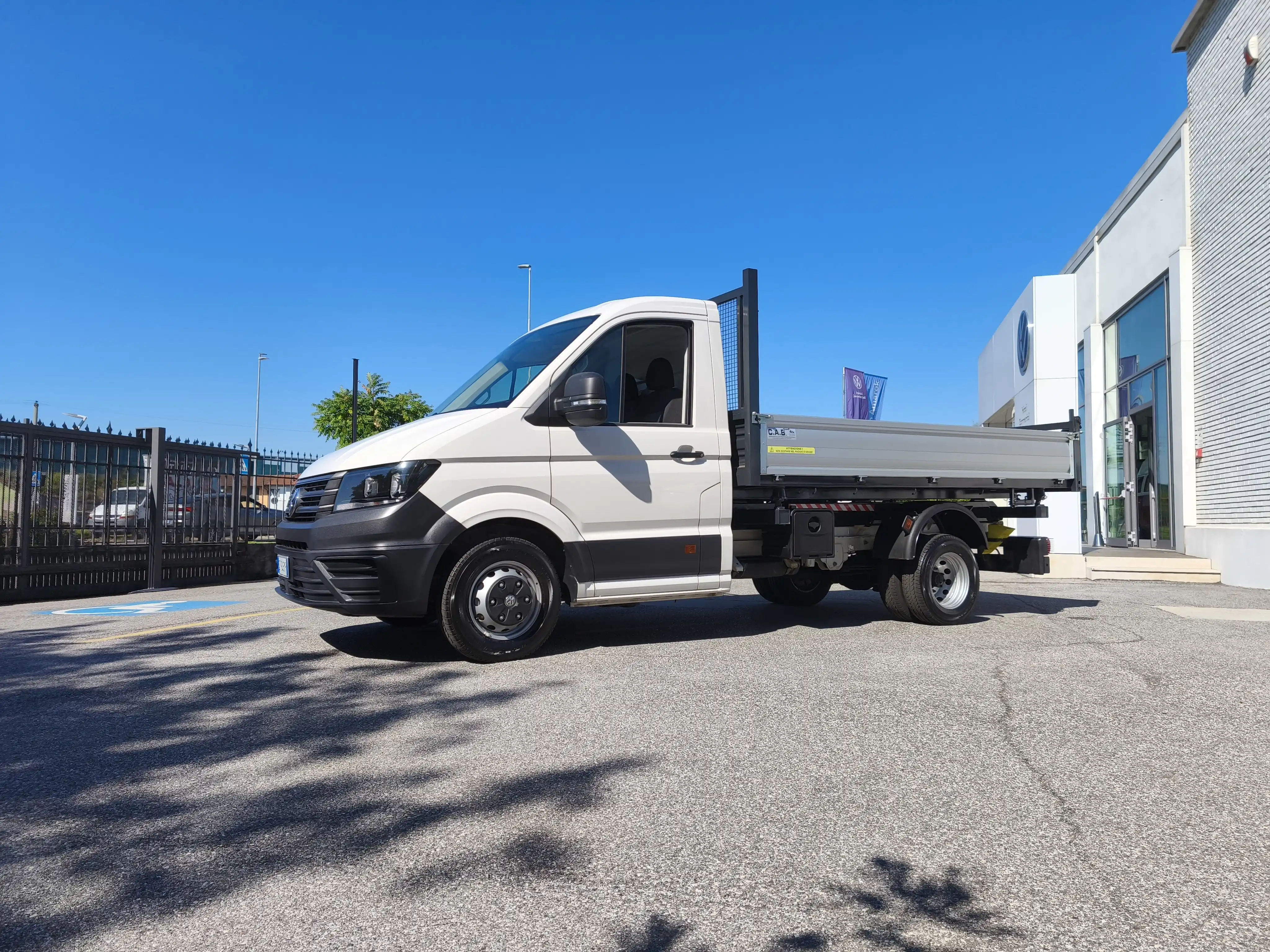 Un camion bianco con un letto piatto parcheggiato davanti a un edificio bianco in una giornata di sole.