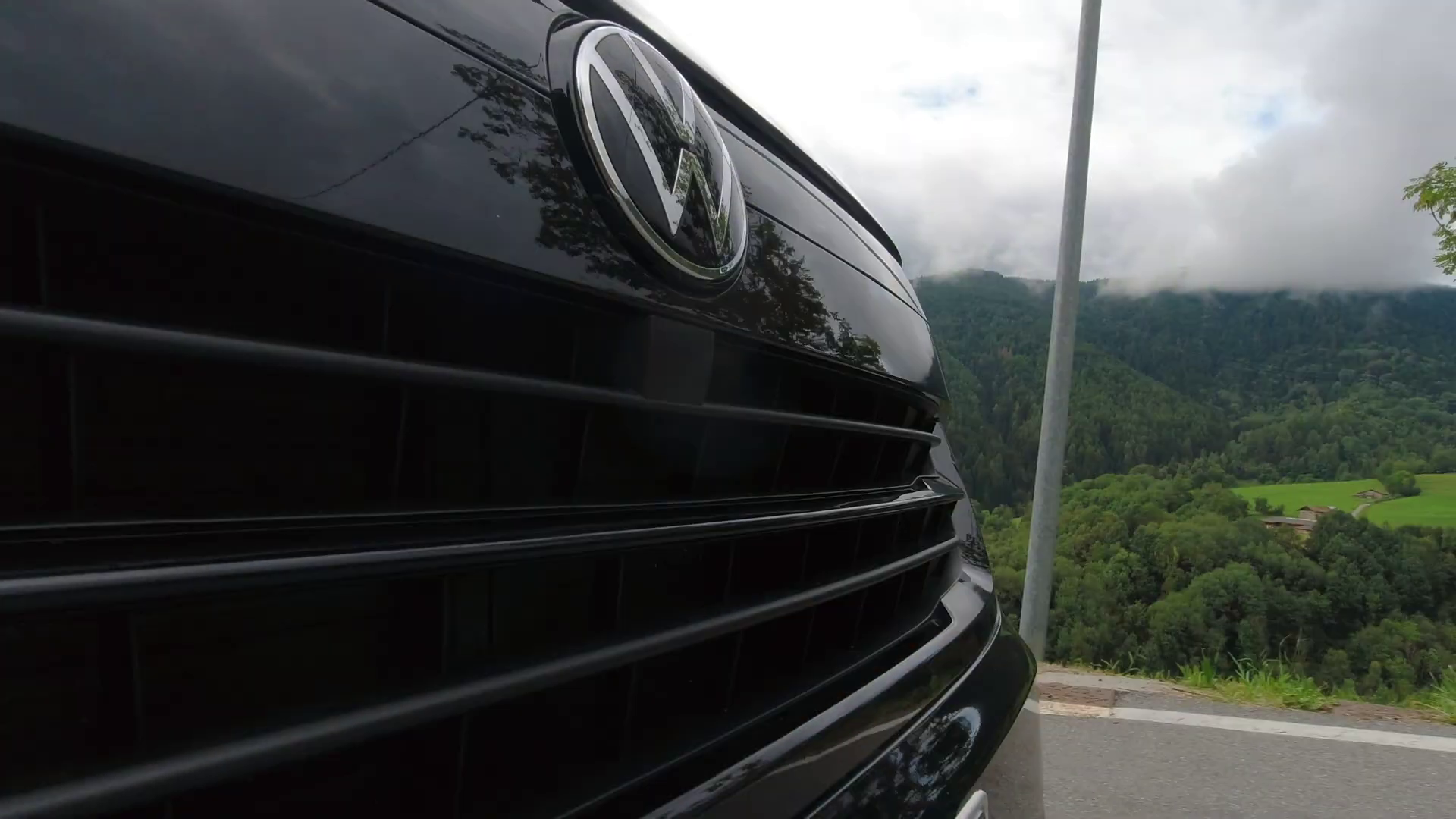 Primo piano della griglia nera e del logo VW di un'auto con montagne sullo sfondo.
