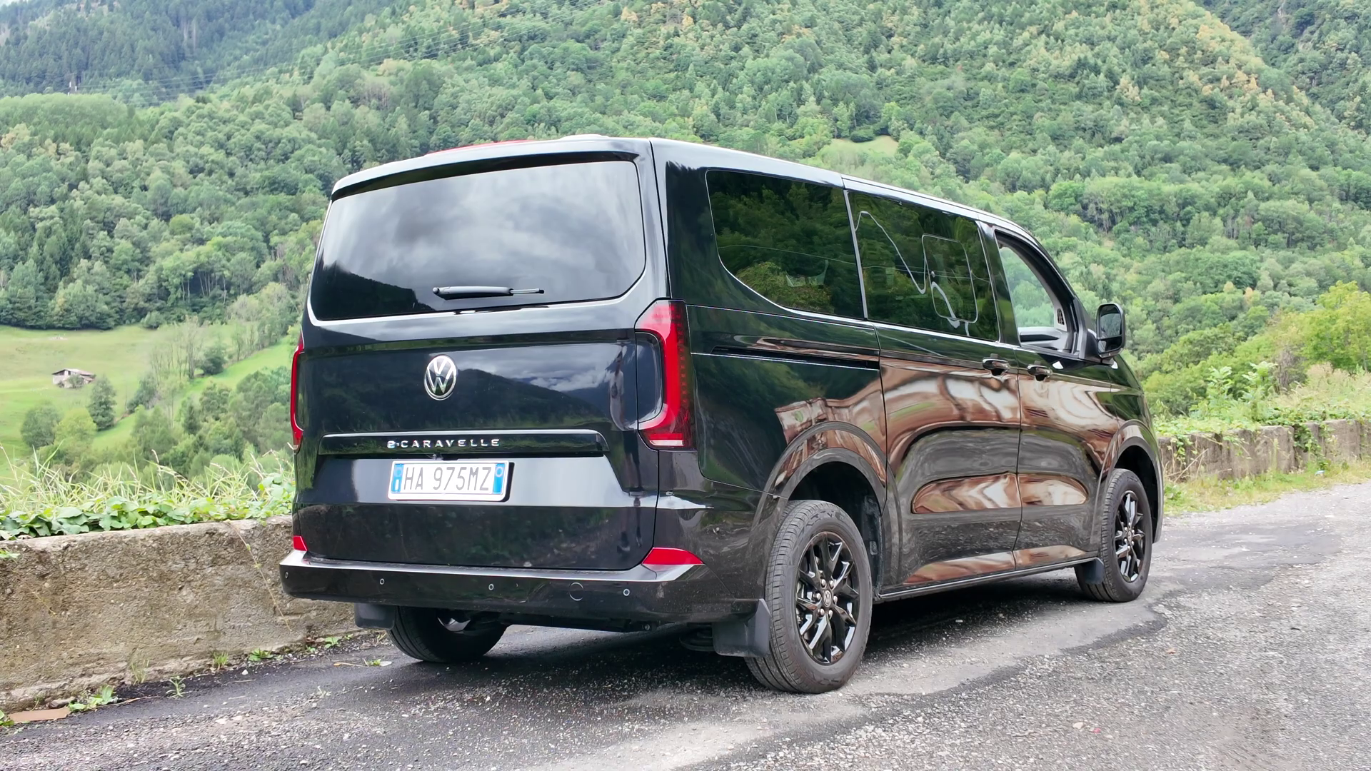 Un Volkswagen E-Caravelle nero su una strada di montagna.