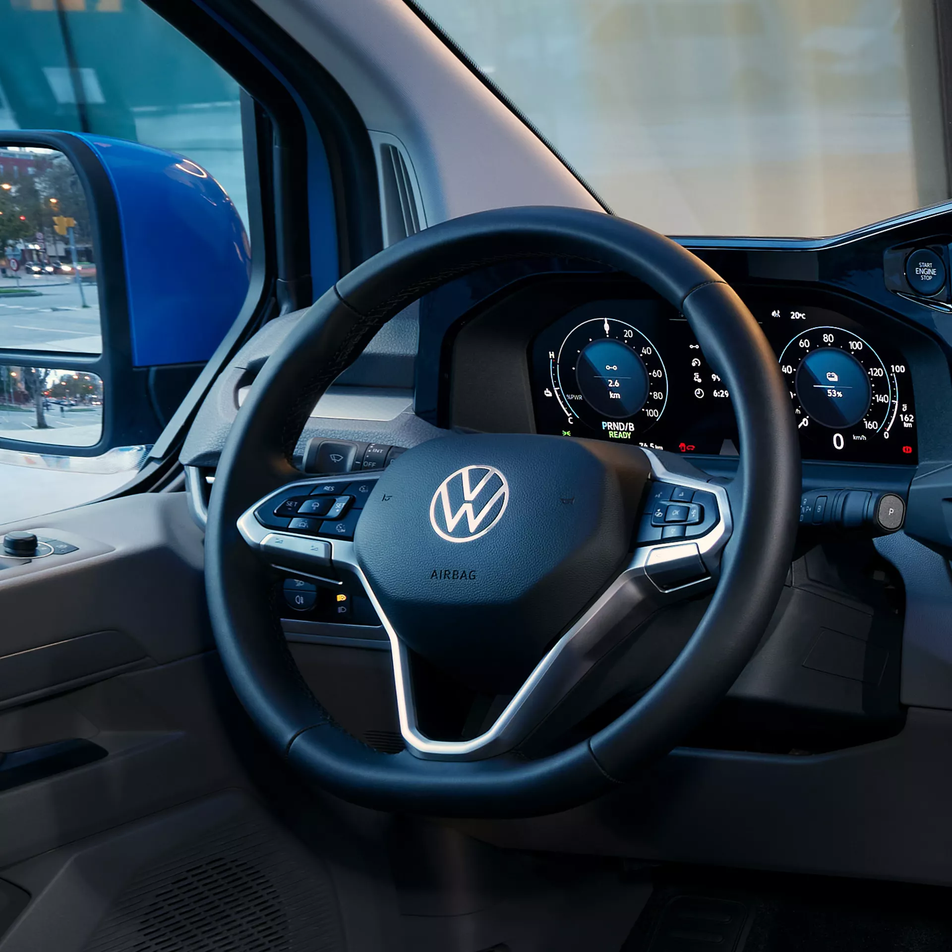L'interno di un veicolo Volkswagen con volante, cruscotto digitale e specchietto retrovisore che mostra una scena di strada.