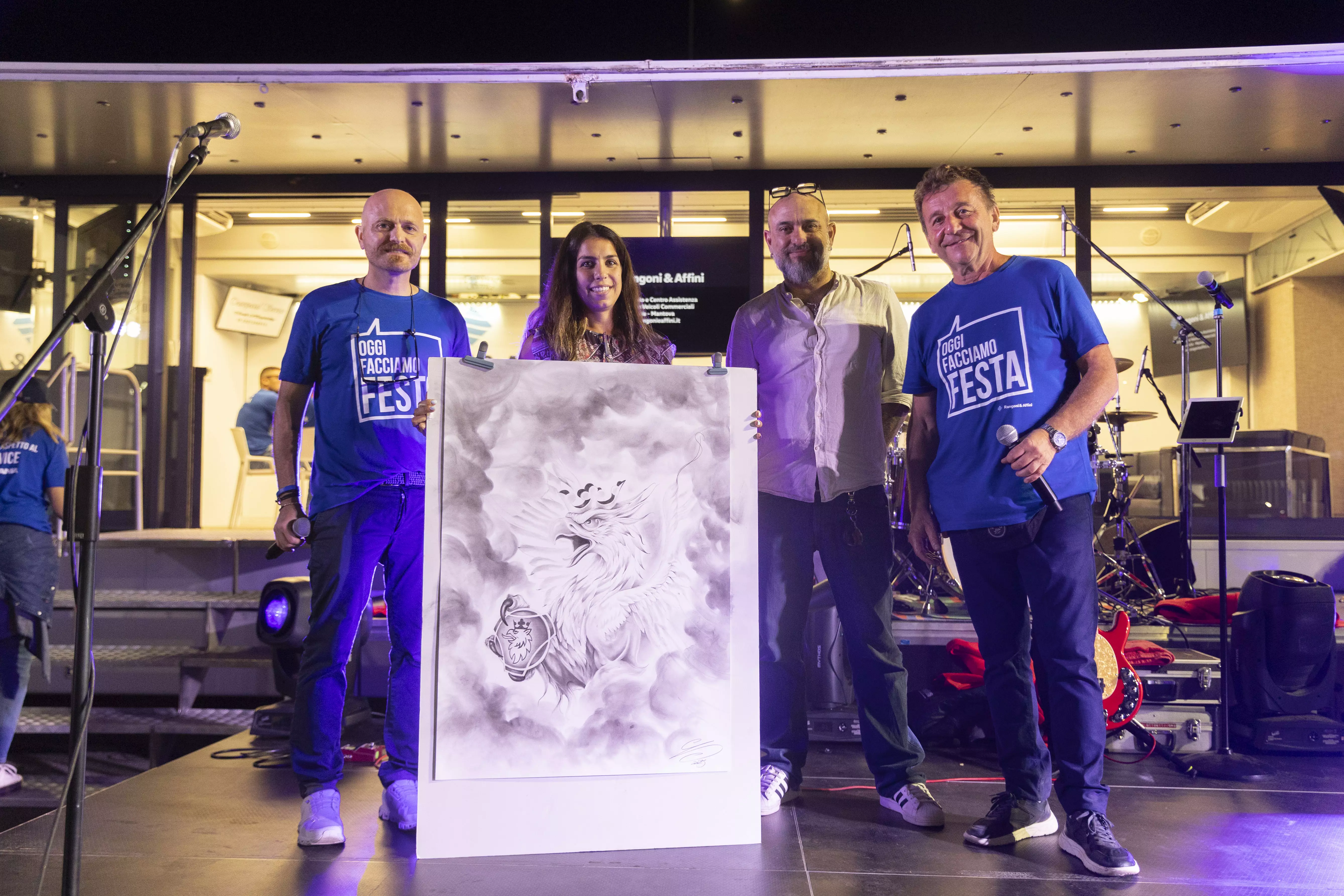 Quattro persone in piedi sul palco che presentano un disegno di una creatura alata.
