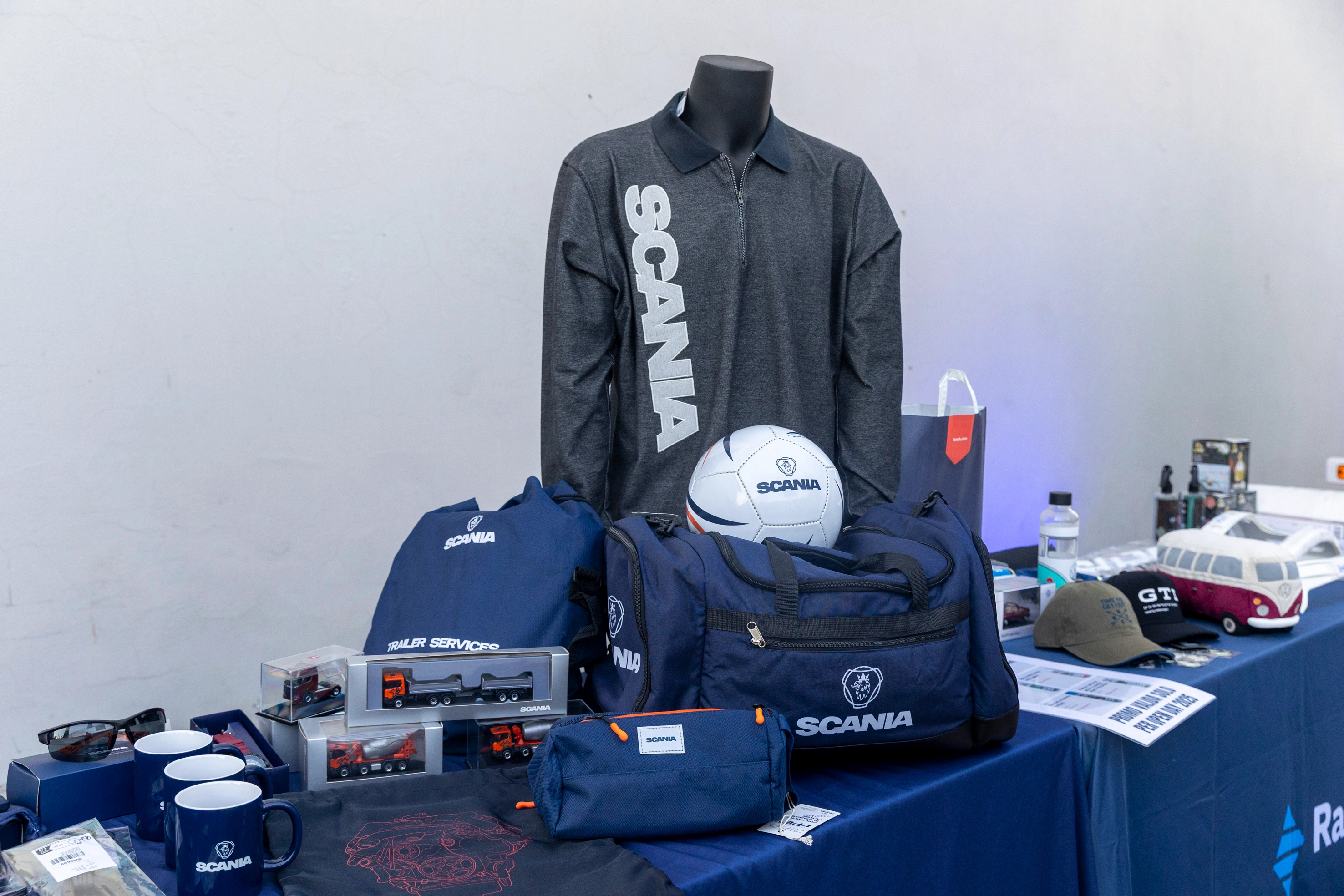 Espositore di articoli promozionali Scania, tra cui magliette, borse, tazze, cappellini e modellini di camion.