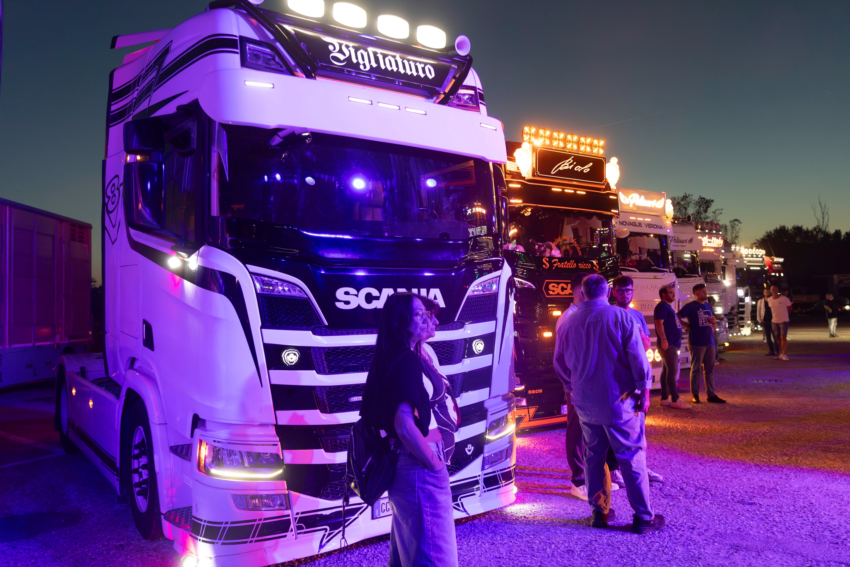 Camion modificati con luci, mostrati a una fiera dove le persone si riuniscono per ammirarli.