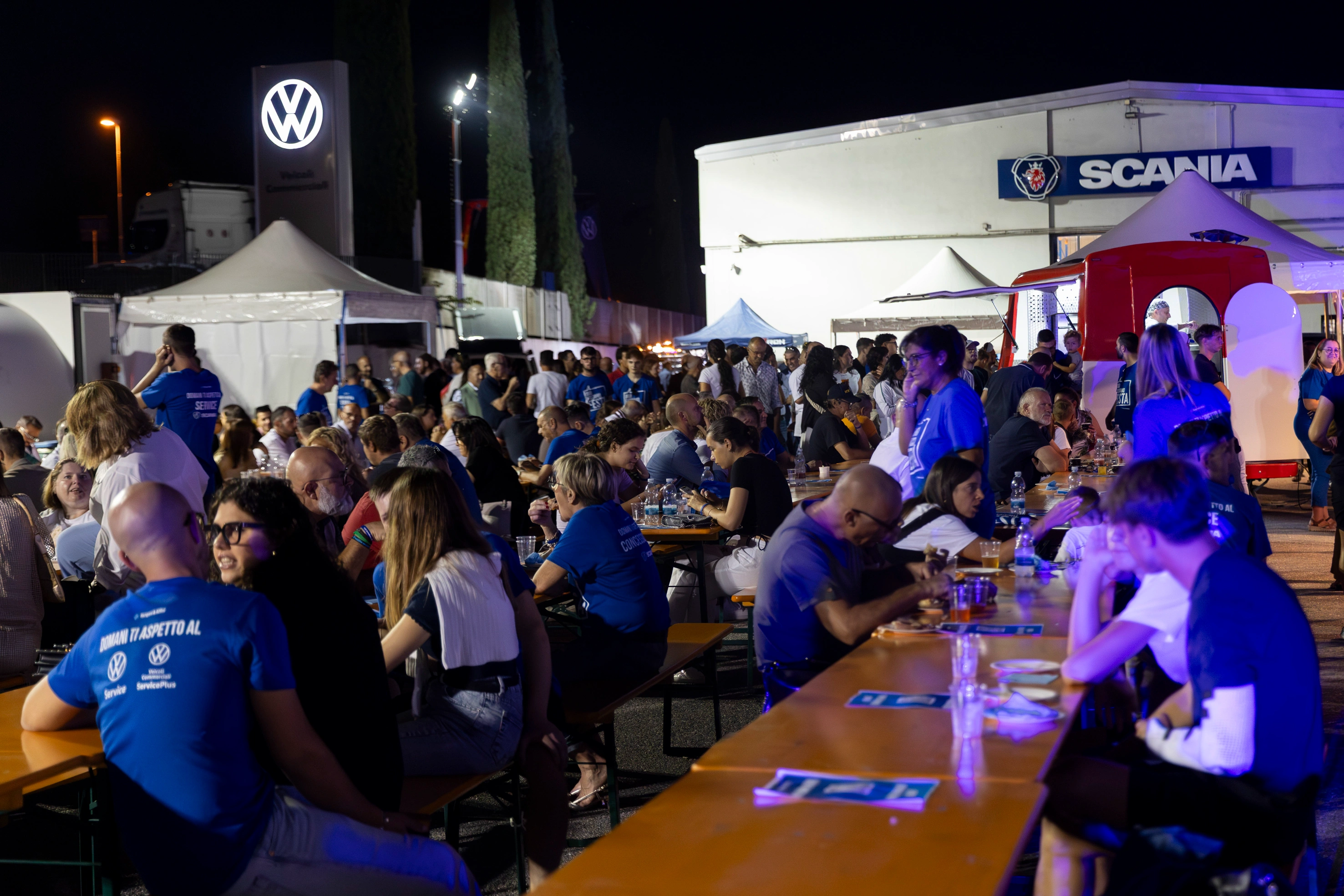 Una folla di persone che cenano a un evento all'aperto di fronte ai loghi Volkswagen e Scania.