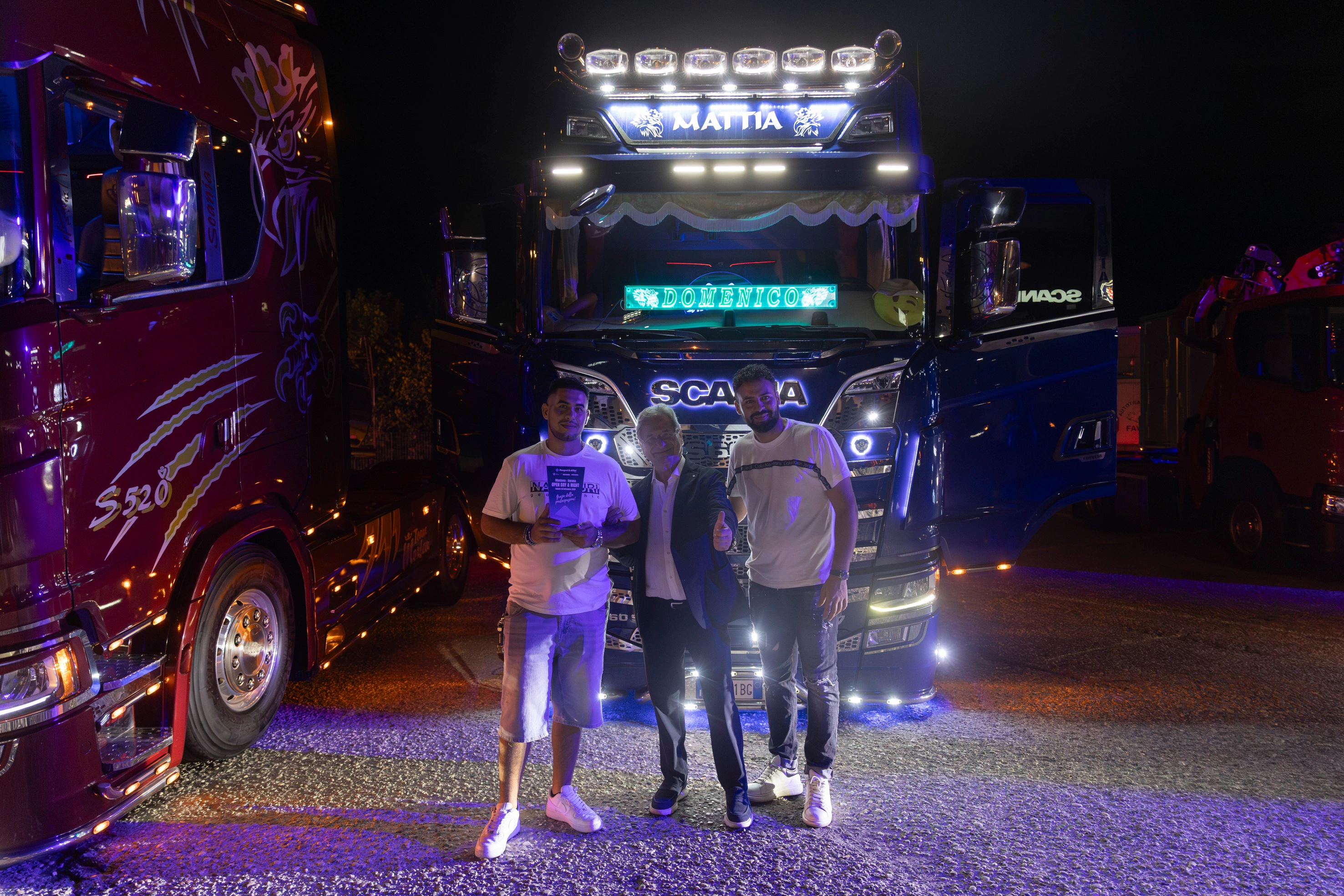 Uomini in posa davanti a camion Scania illuminati.