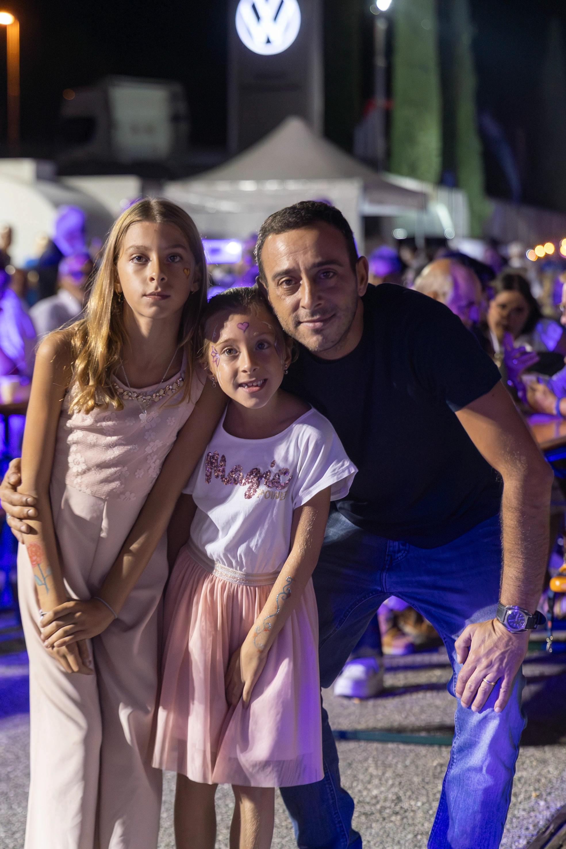 Un uomo e due bambine sorridono alla macchina fotografica di notte.
