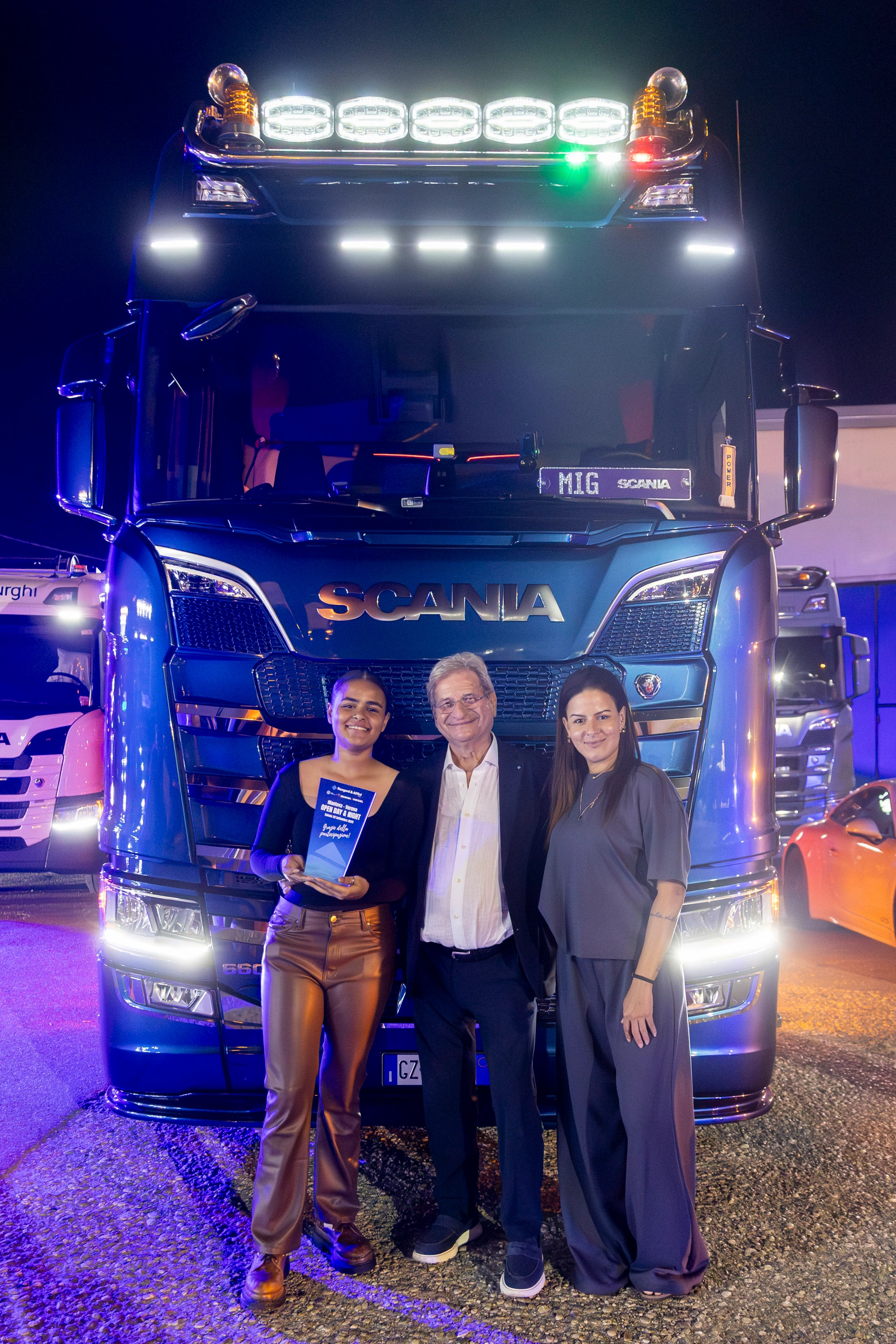 Tre persone posano davanti a un camion SCANIA blu.