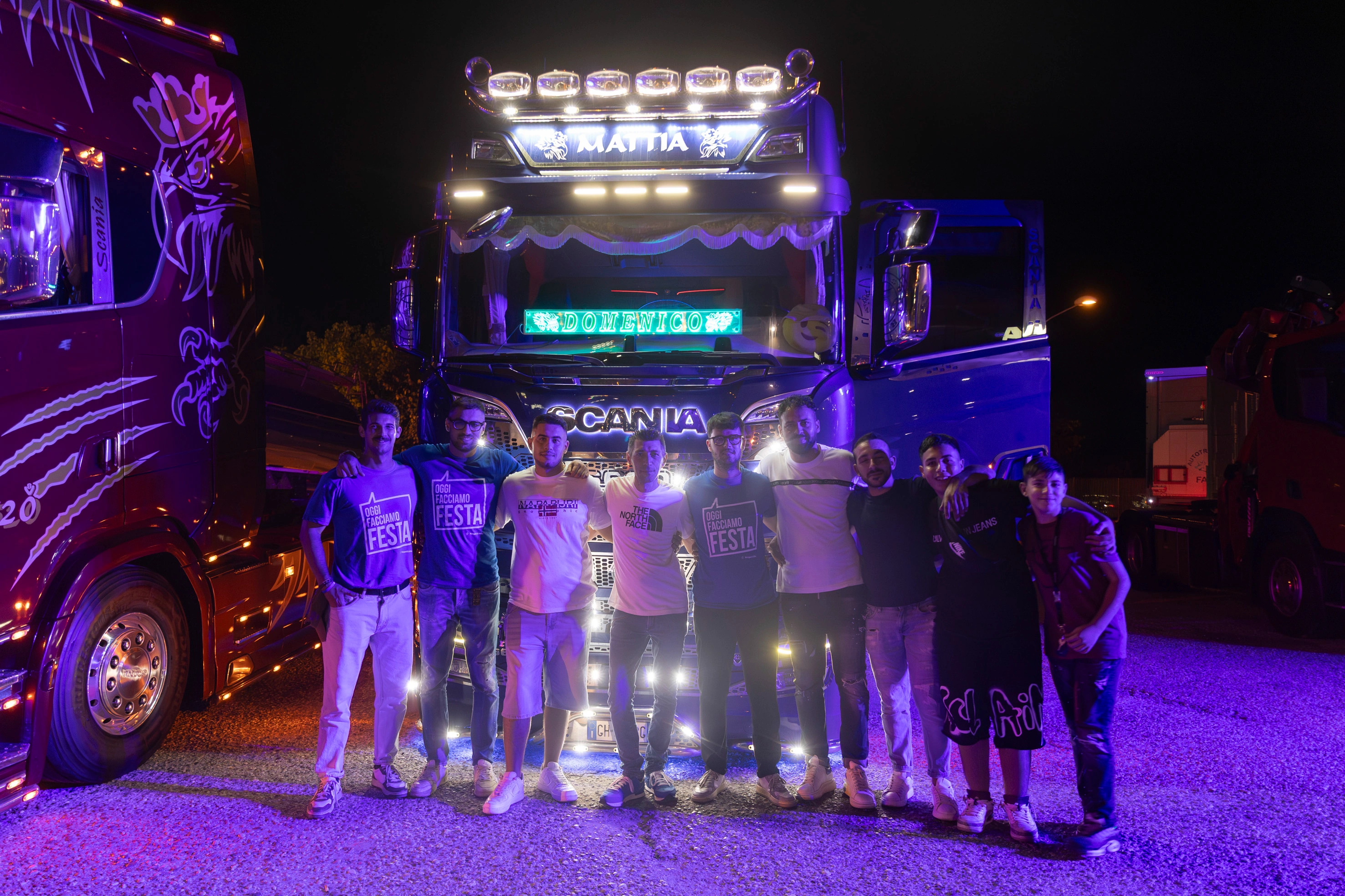 Un gruppo di uomini posa davanti a un camion Scania decorato con luci.