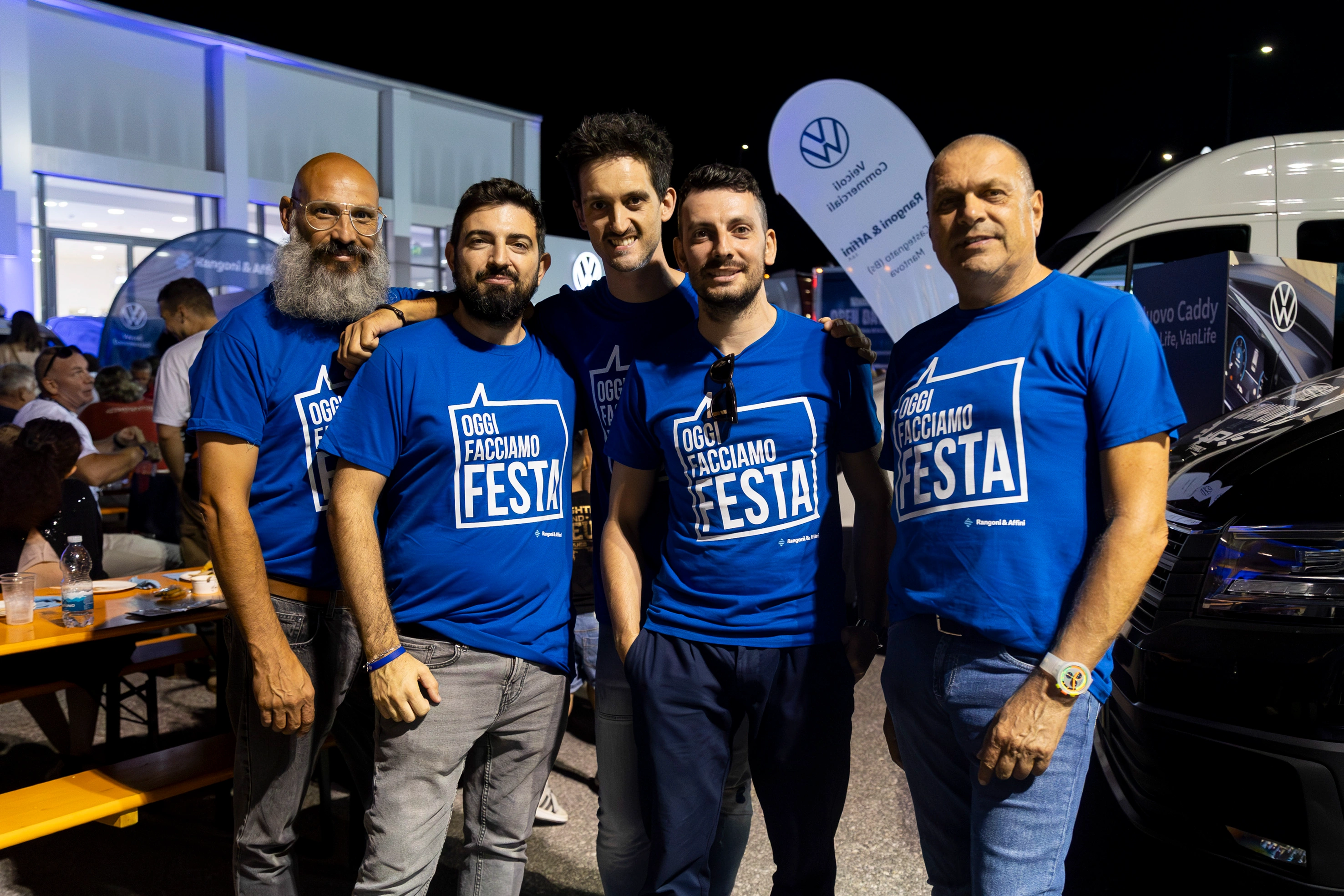 Un gruppo di cinque uomini in fila, che indossano magliette blu con la scritta "OGGI FACCIAMO FESTA".