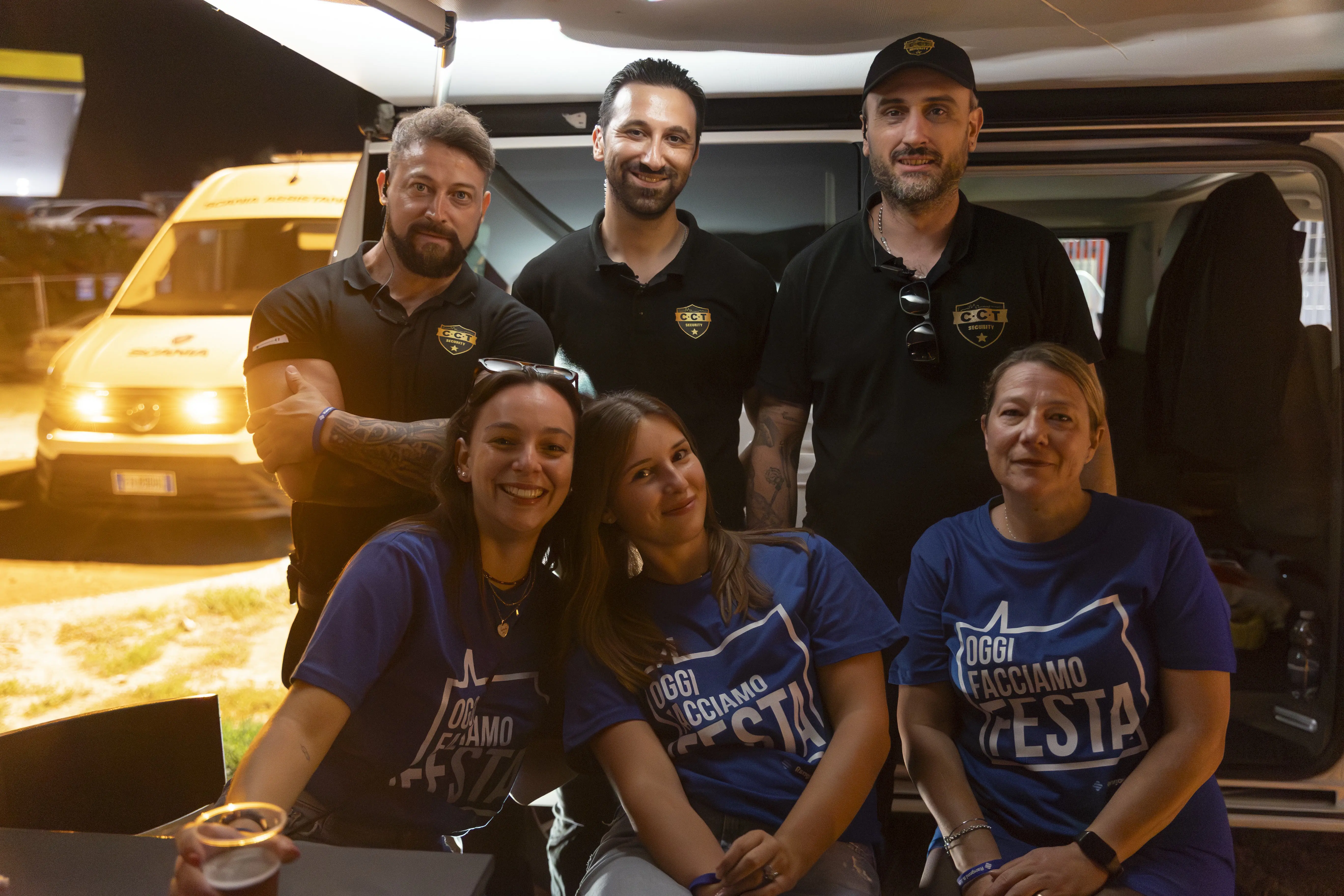 Un gruppo di sei persone posa per una foto di gruppo all'aperto, con un furgone bianco sullo sfondo. Tutti sorridono.