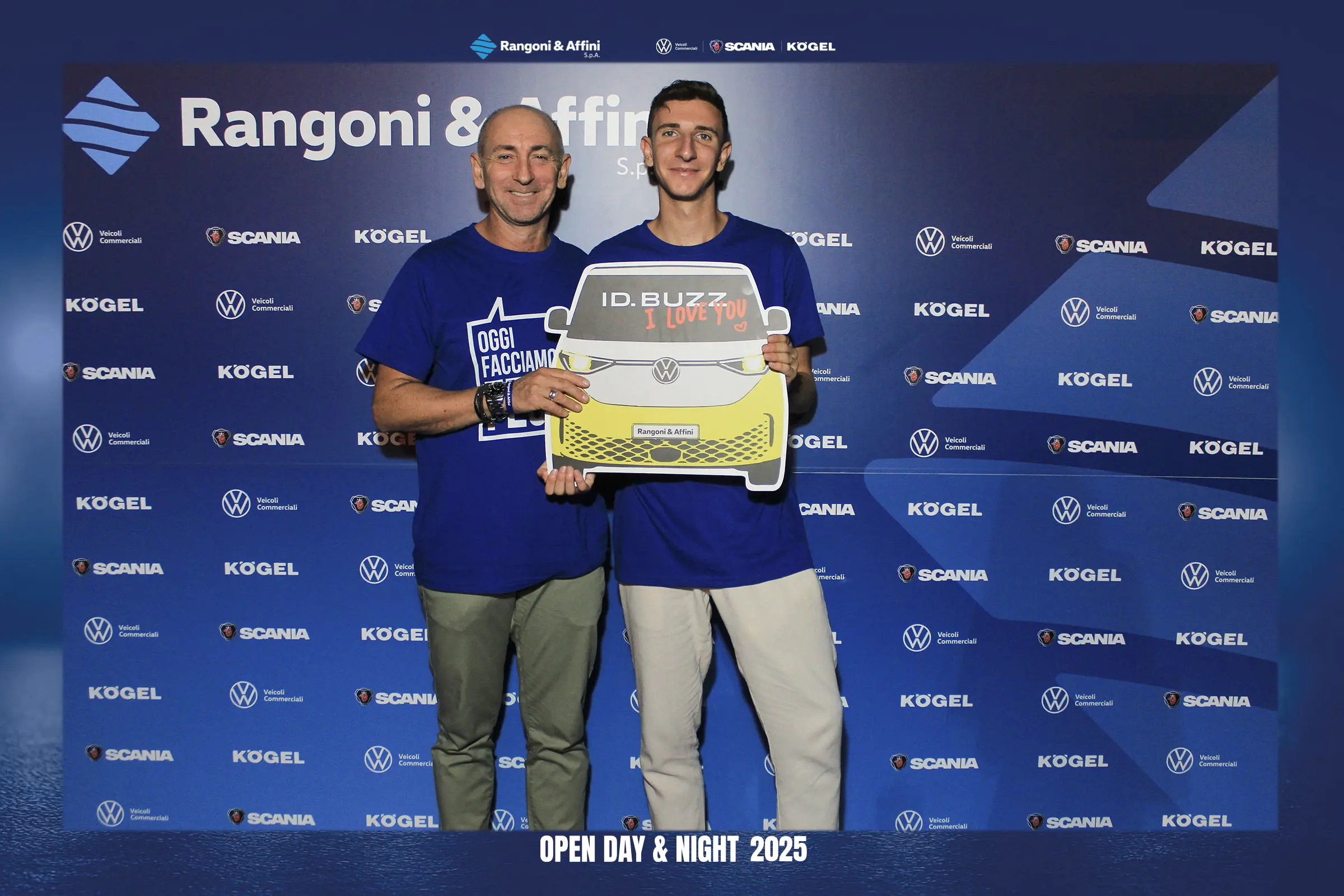 Due uomini posano davanti a uno sfondo di marca tenendo in mano un cartello a forma di furgone VW ID.Buzz.