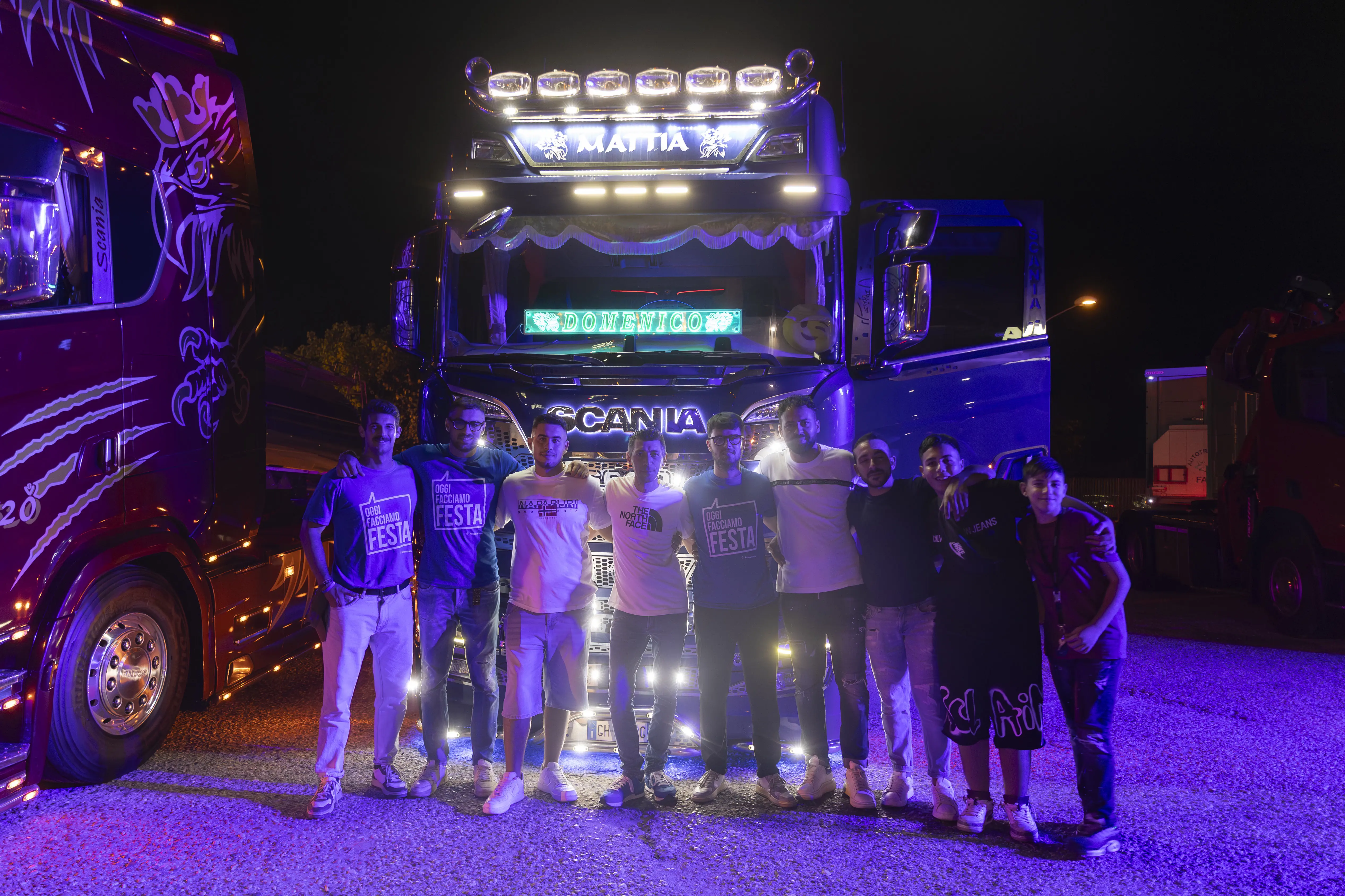 Un gruppo di persone si riunisce di fronte a due camion illuminati per una foto di gruppo notturna.