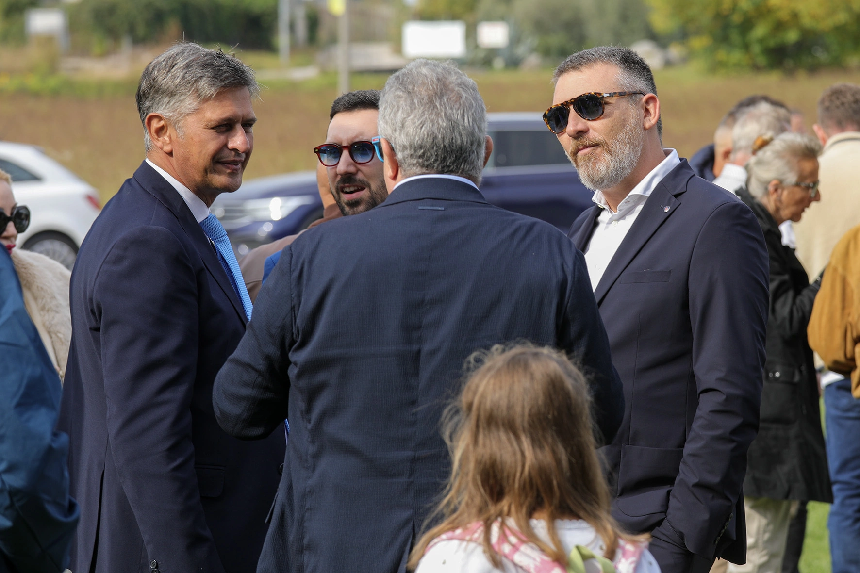 Un gruppo di persone vestite con abiti formali in piedi all'aperto in una giornata di sole.