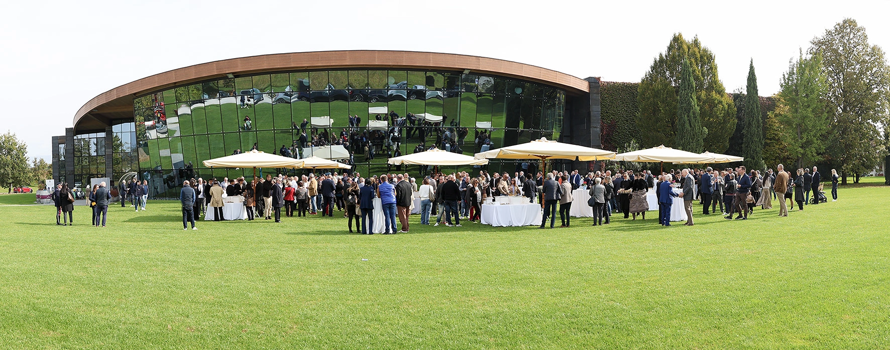 Una folla di persone si riunisce sul prato fuori da un edificio moderno per un evento.