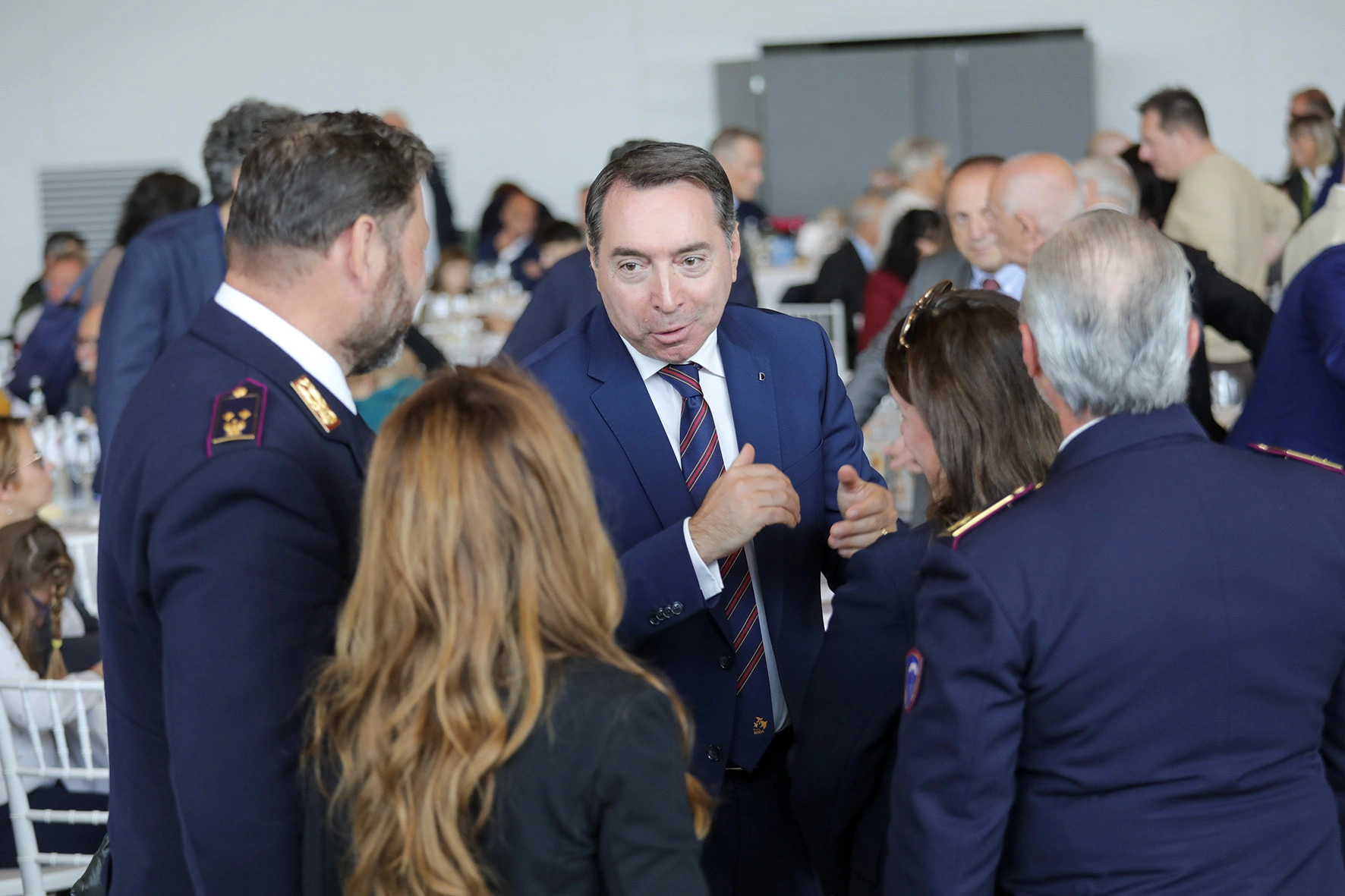 Uomo in giacca blu che parla con persone in uniforme.