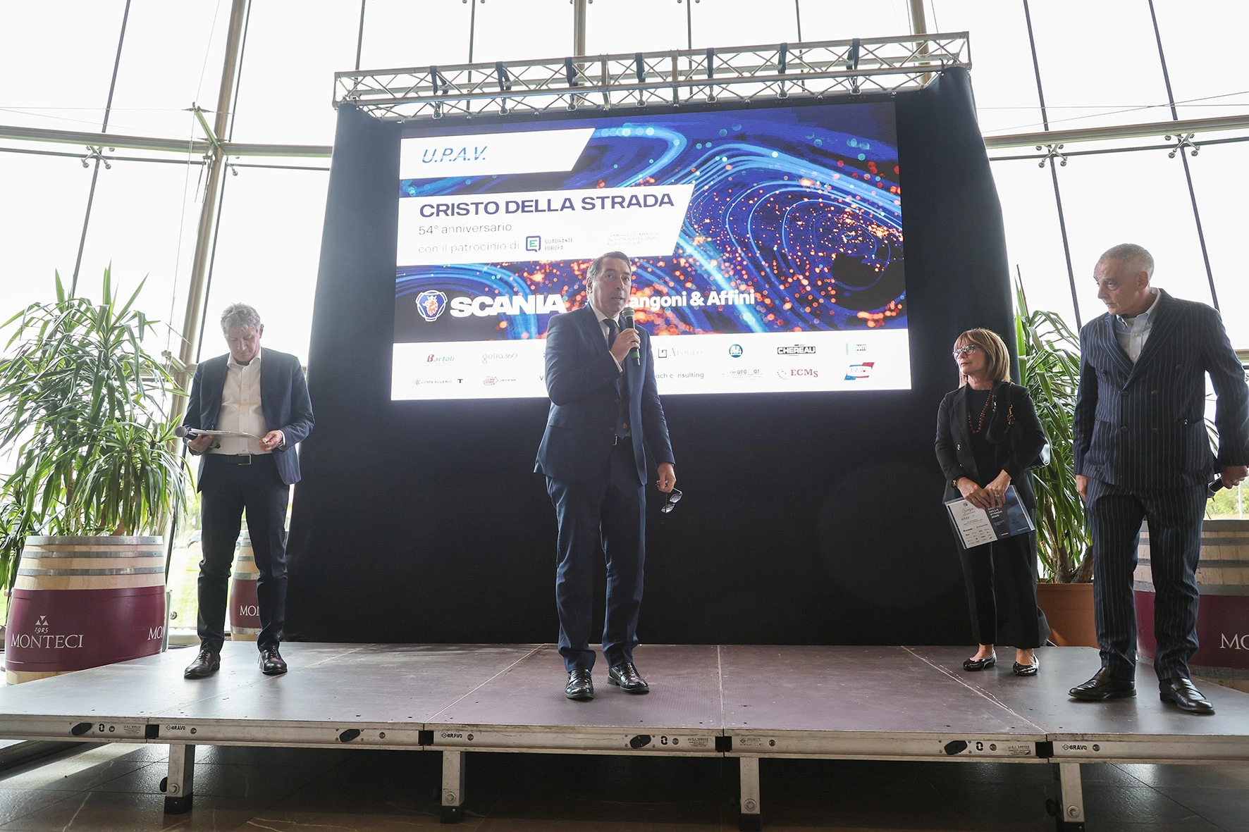 Persone in piedi su un palco con uno schermo sullo sfondo.