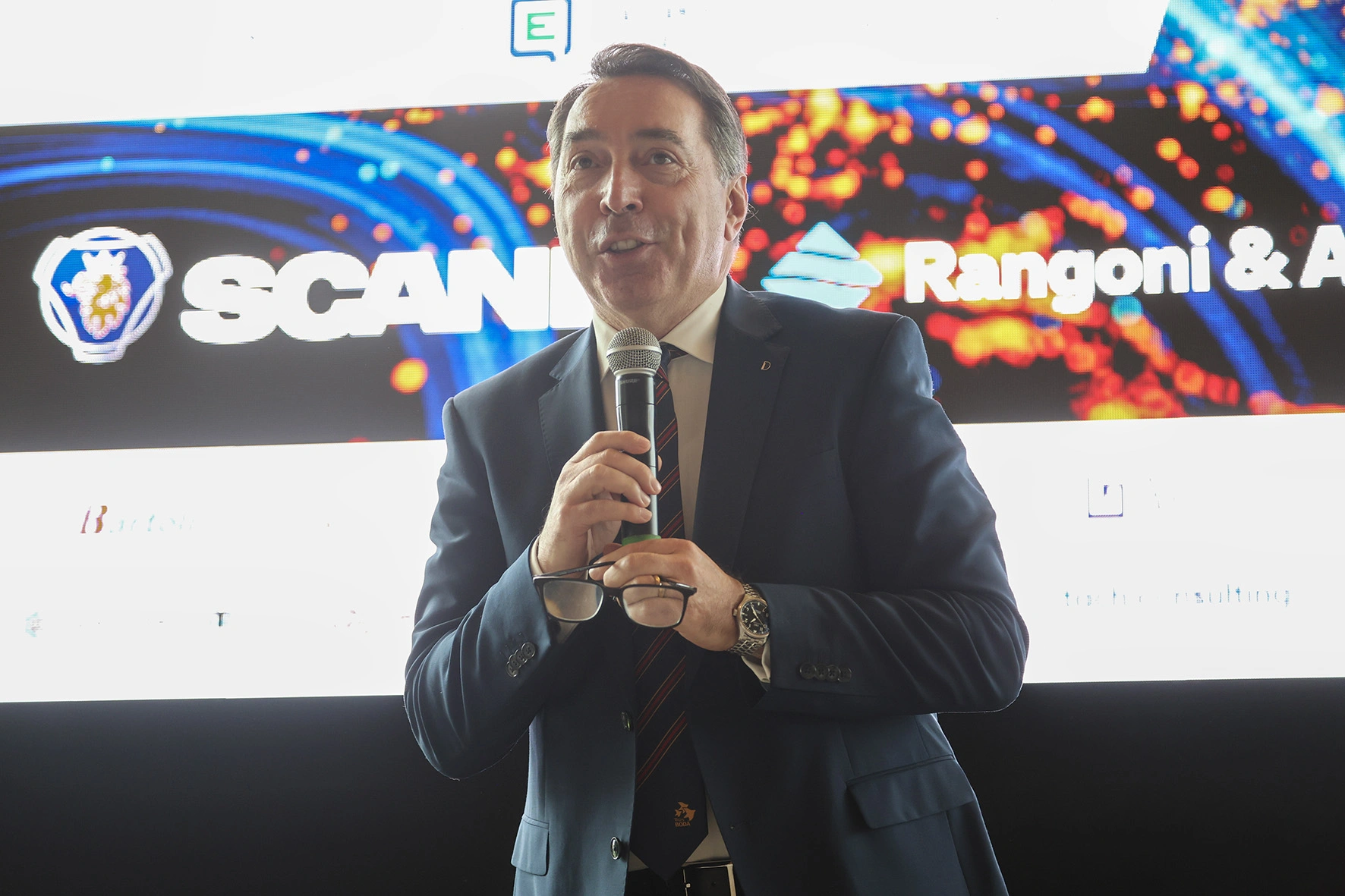 Uomo in giacca e cravatta che parla al microfono.