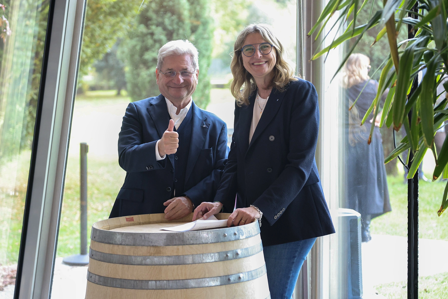 Due persone in piedi vicino a una botte di vino che sorridono.