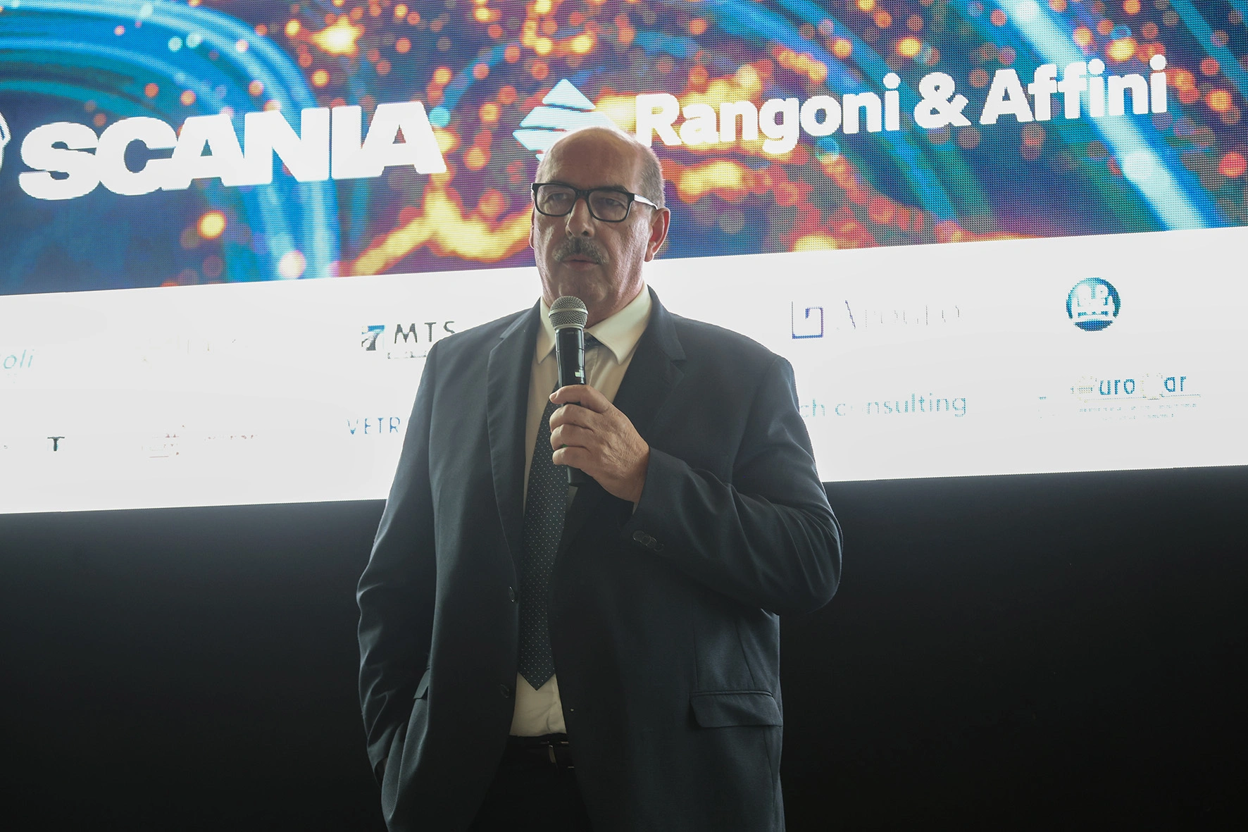 Un uomo con una giacca che parla al microfono.