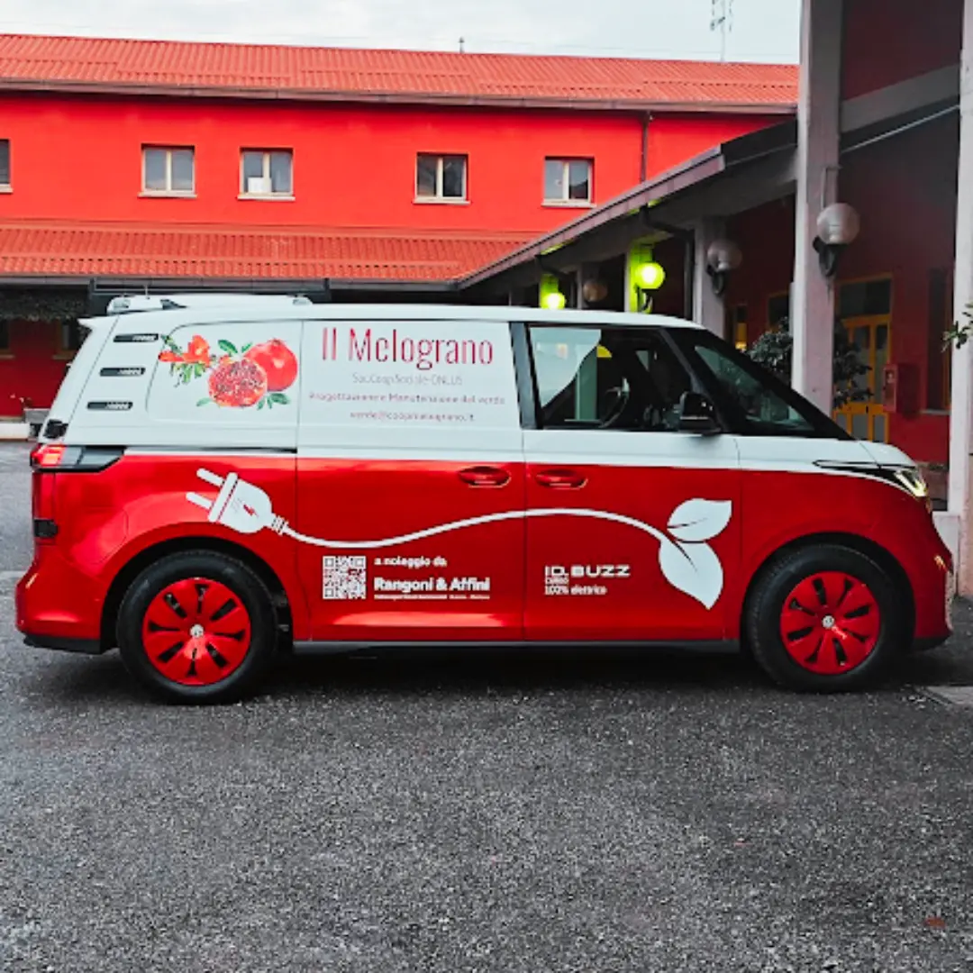 Un furgone bianco e rosso con la scritta "II Melograno" parcheggiato di fronte a un edificio rosso.