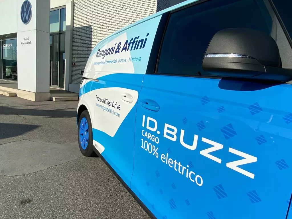 Un furgone Volkswagen ID. Buzz Cargo 100% elettrico, con livrea blu e bianca, parcheggiato davanti a una concessionaria.