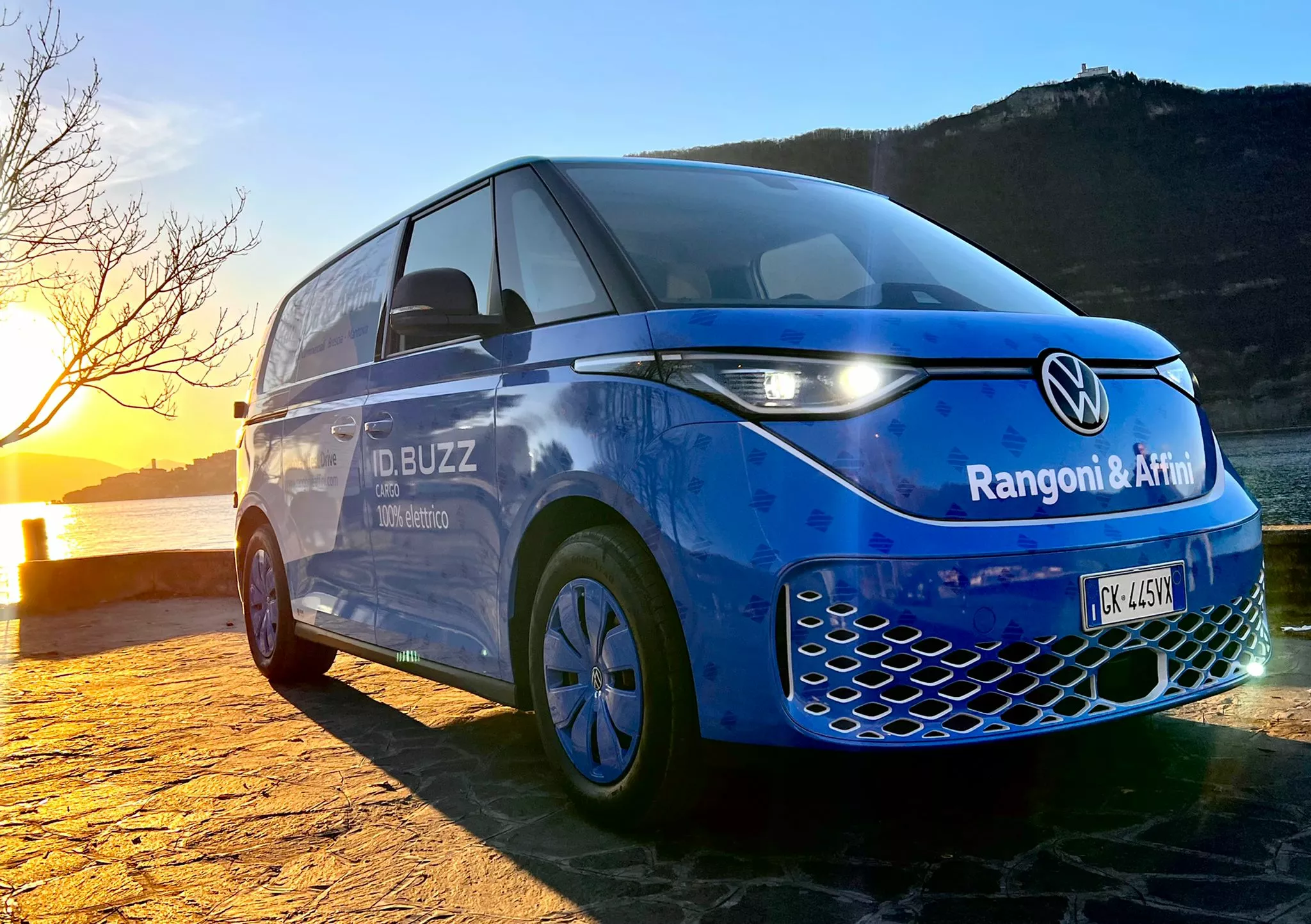 Un furgone VW ID.Buzz Cargo blu parcheggiato con il sole al tramonto sullo sfondo.