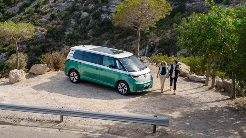 Un'auto verde elettrica parcheggiata mentre due persone camminano di lato.