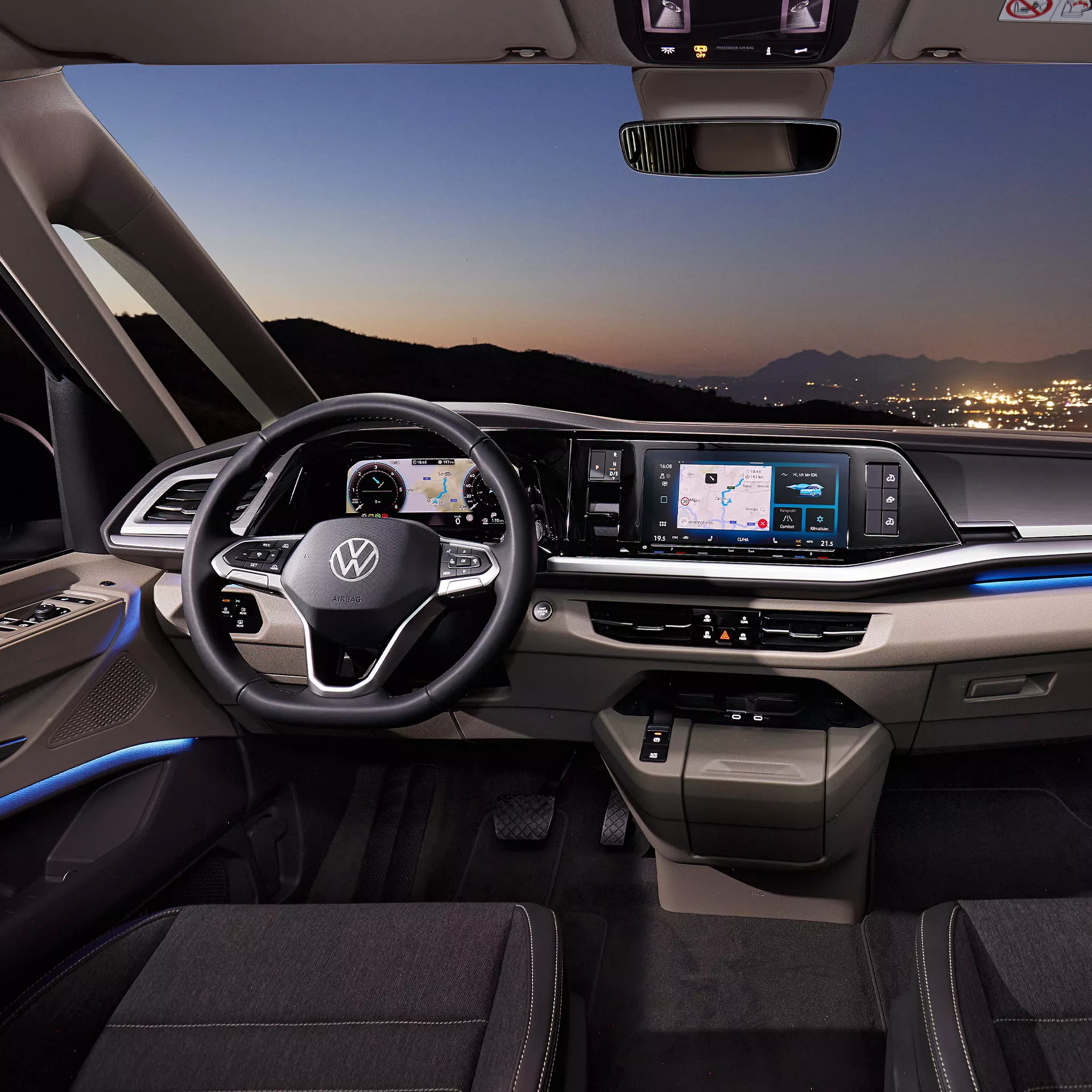 Interni di un'auto con cruscotto digitale e vista sul paesaggio al tramonto.